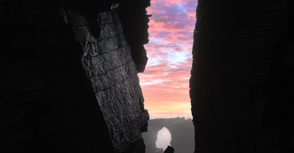 A view of a colorful sunset through a crack in dark, rocky formations.