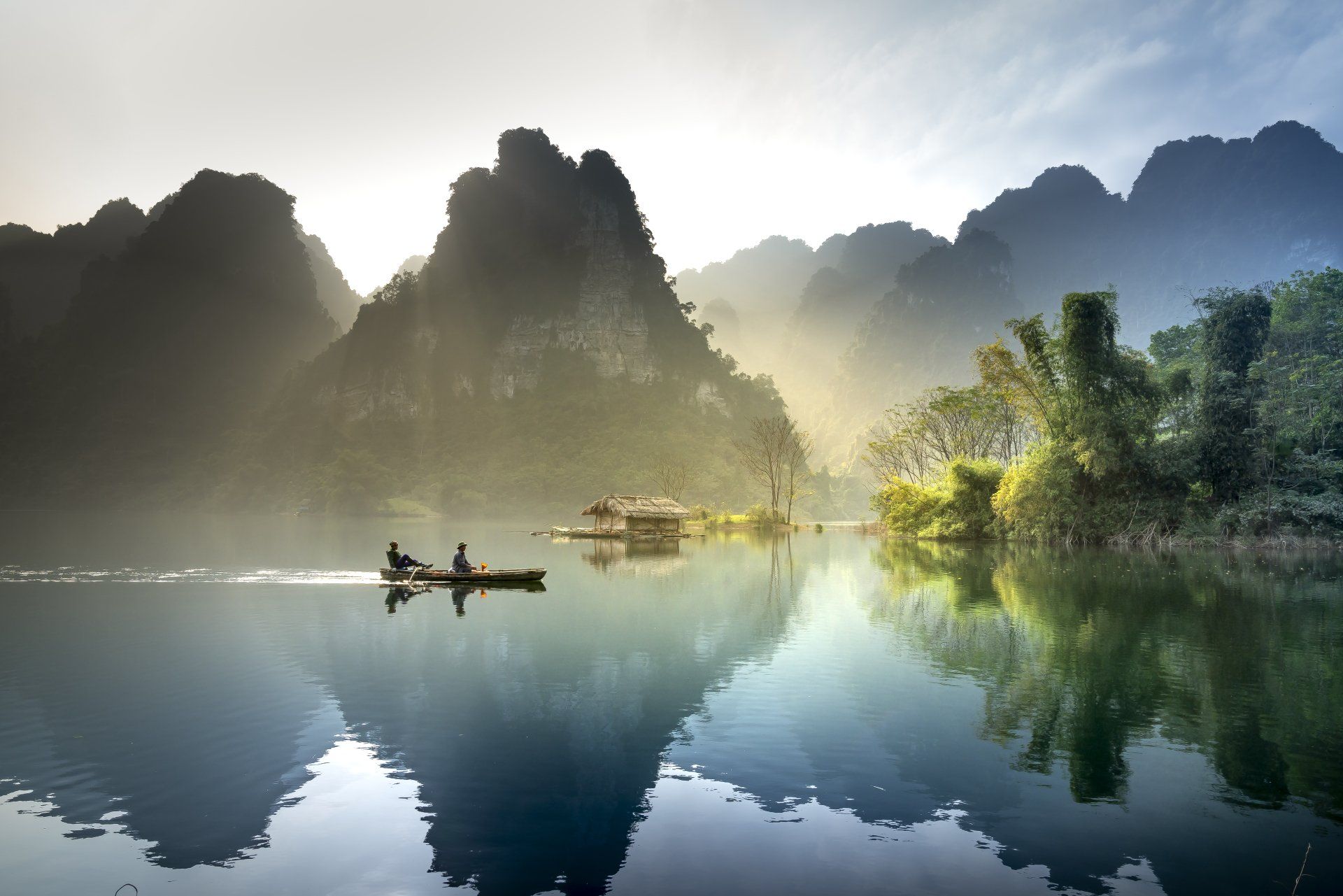 Two people are rowing a boat on a lake with mountains in the background.