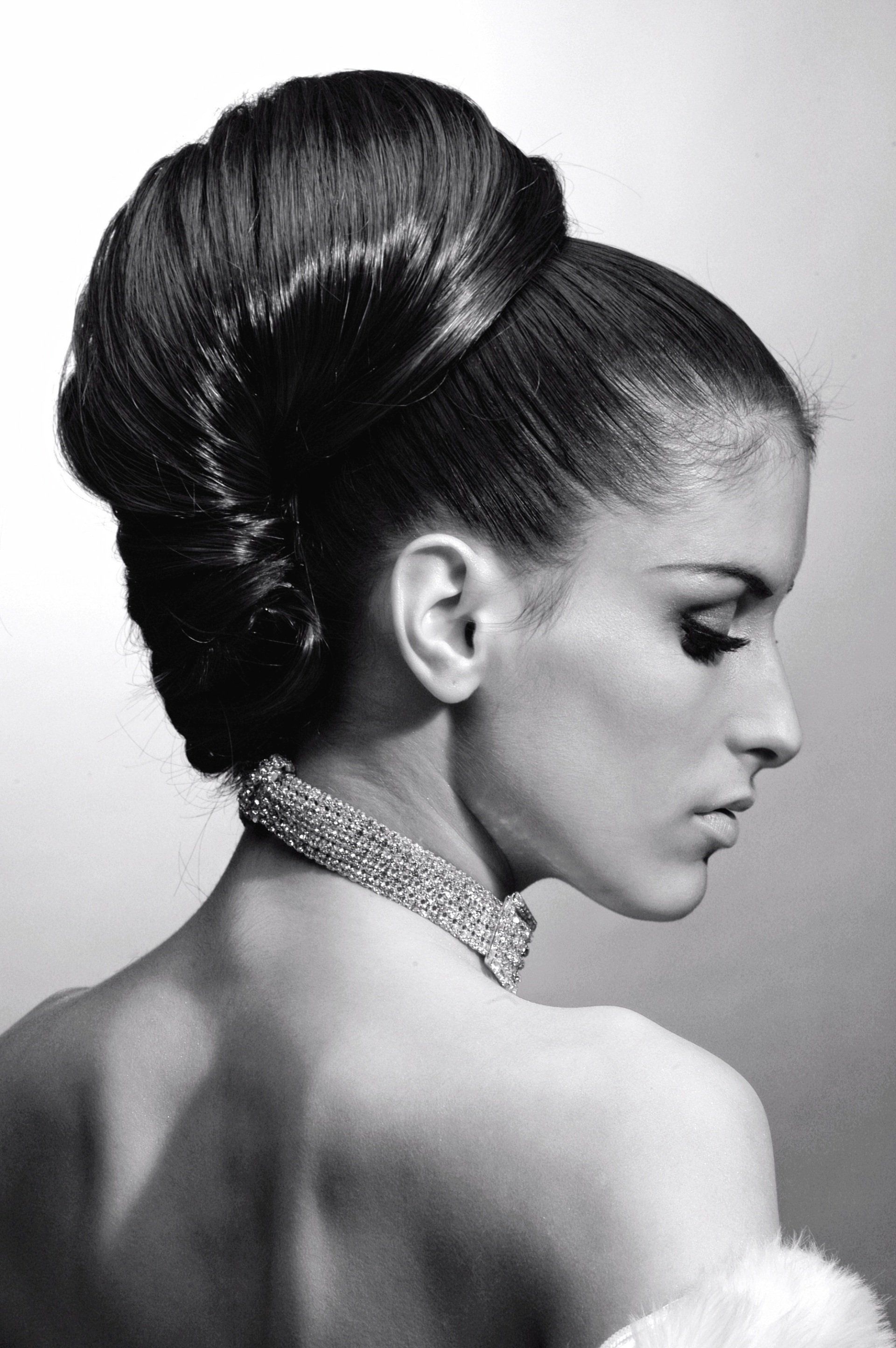Woman with elegant updo hairstyle, wearing a jeweled necklace, looking down. Black and white.