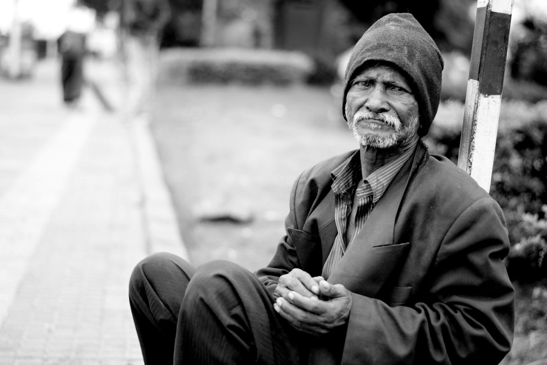 Uma foto em preto e branco de um homem idoso sentado na calçada.