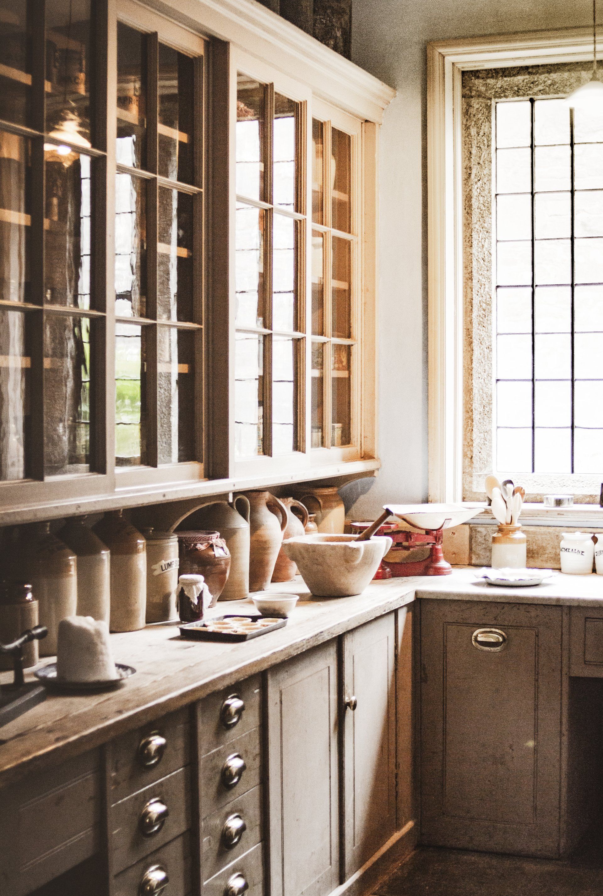 Sunlit kitchen with cabinets, pottery on the counter, and tall windows in a rustic interior