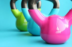 Gyms, Sports, Coaching and Personal Trainers Three different colored kettlebells are lined up on a blue surface.