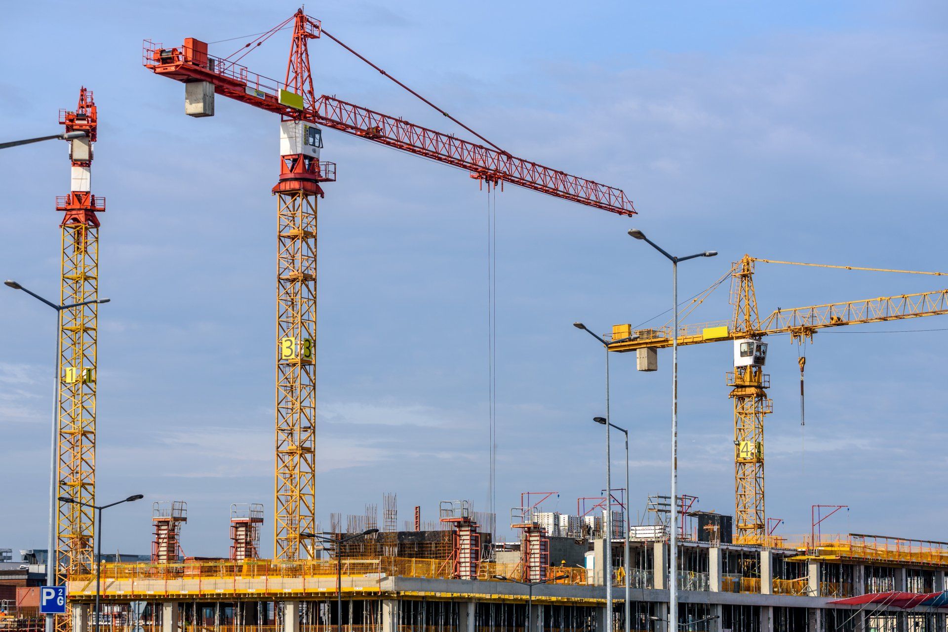 Baustelle mit hohen gelben und roten Turmdrehkranen vor blauem Himmel