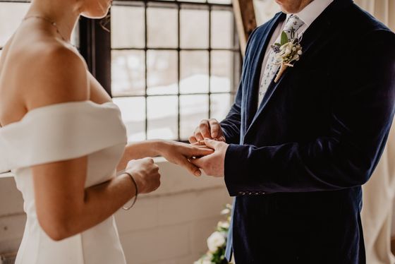 A bride and groom are getting married and the bride is putting the ring on the groom 's finger.