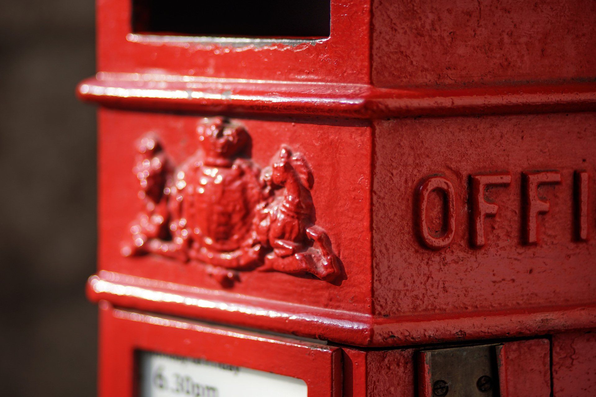 Een close-up van een felrode brievenbus van de Britse Royal Mail met een reliëf van het koninklijk wapen.