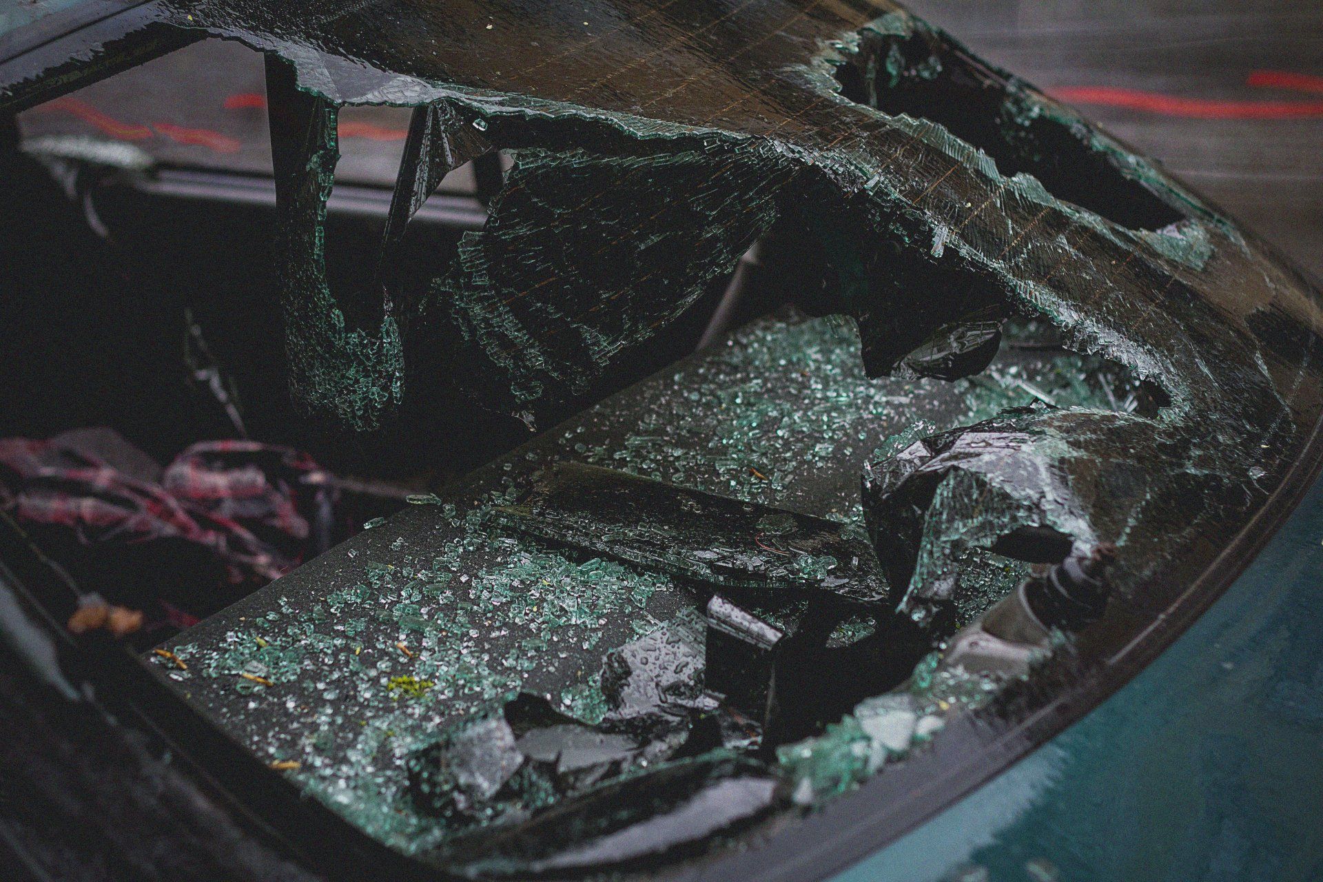Shattered rear windshield of a green car, glass fragments scattered.