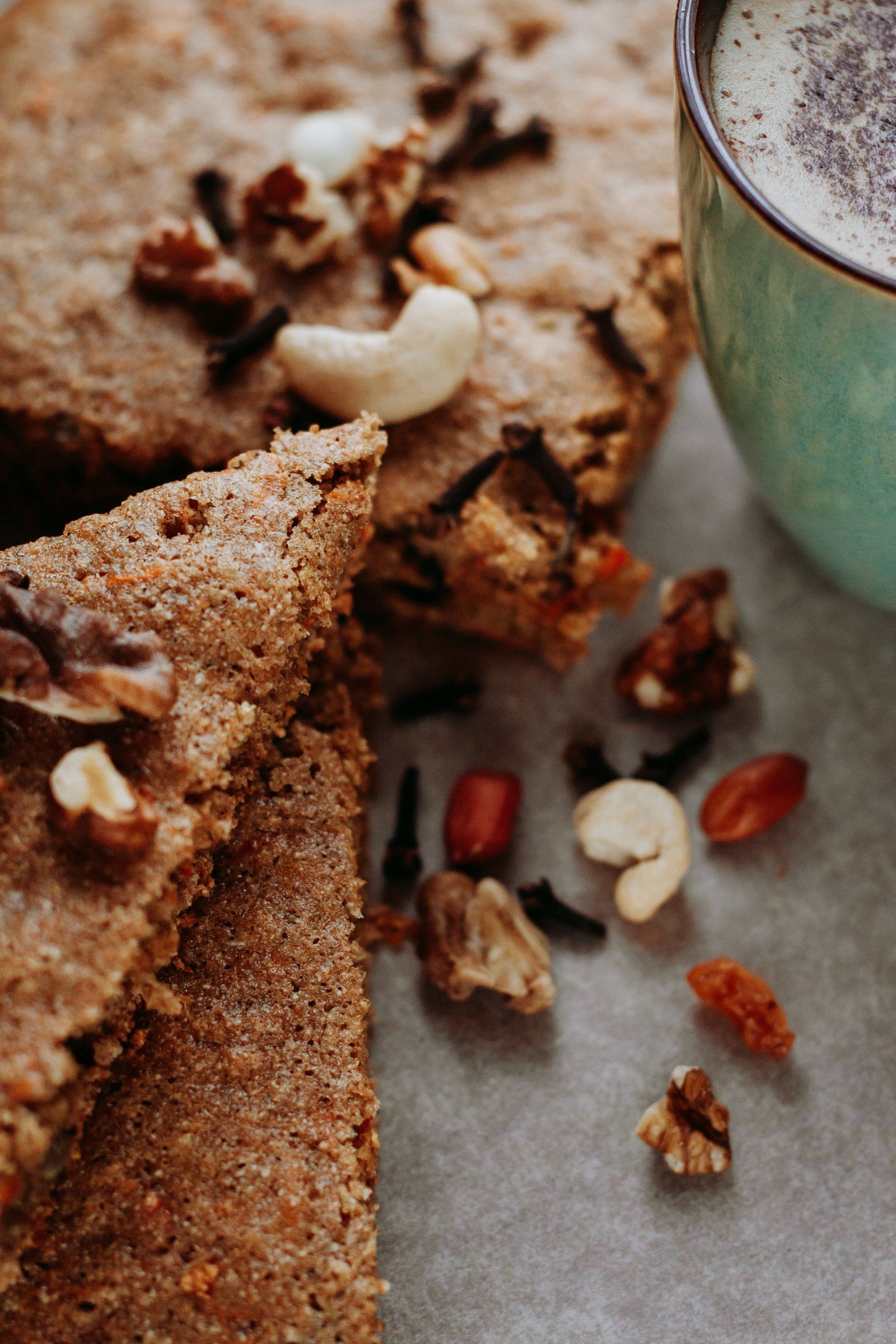 Close-up of baked goods with nuts and spices, next to a teal mug of a milky drink.