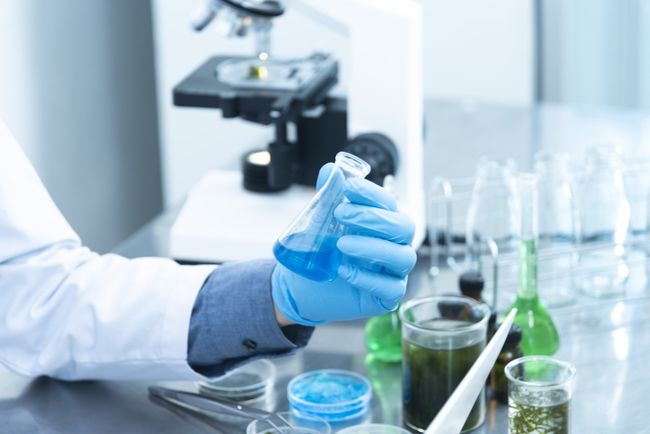 Hope Through Business A scientist is holding a beaker of blue liquid in a laboratory.