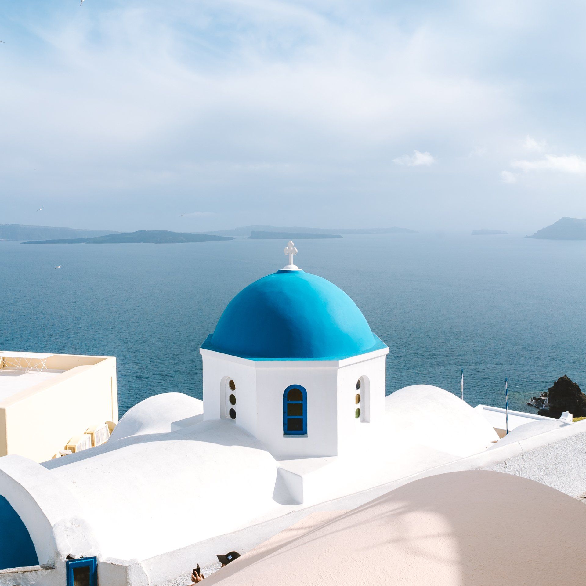 Kirche mit blauer Kuppel auf einem weißen Gebäude mit Blick auf die Ägäis, Santorin, Griechenland.