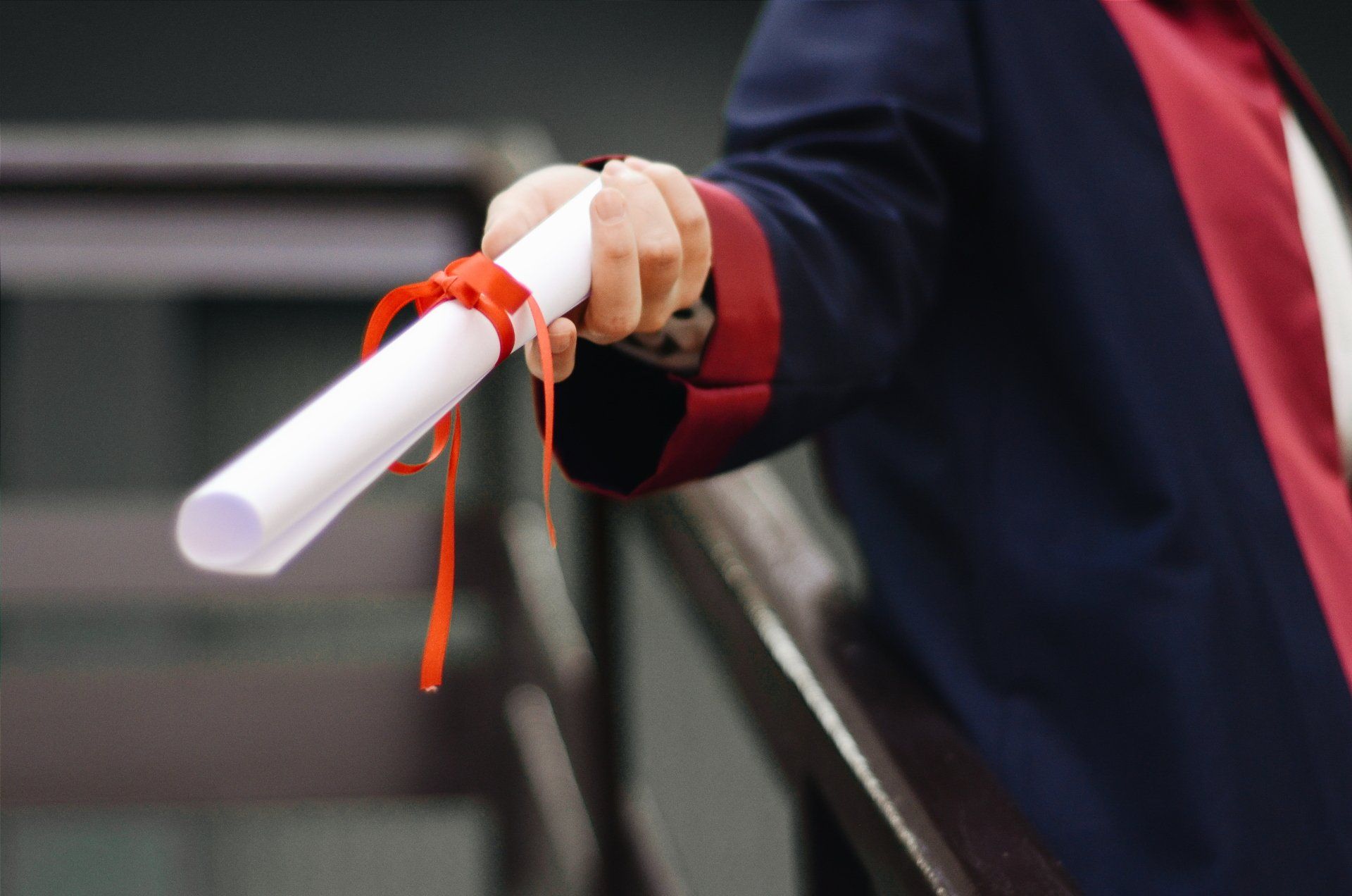A person is holding a diploma with a red ribbon around it.