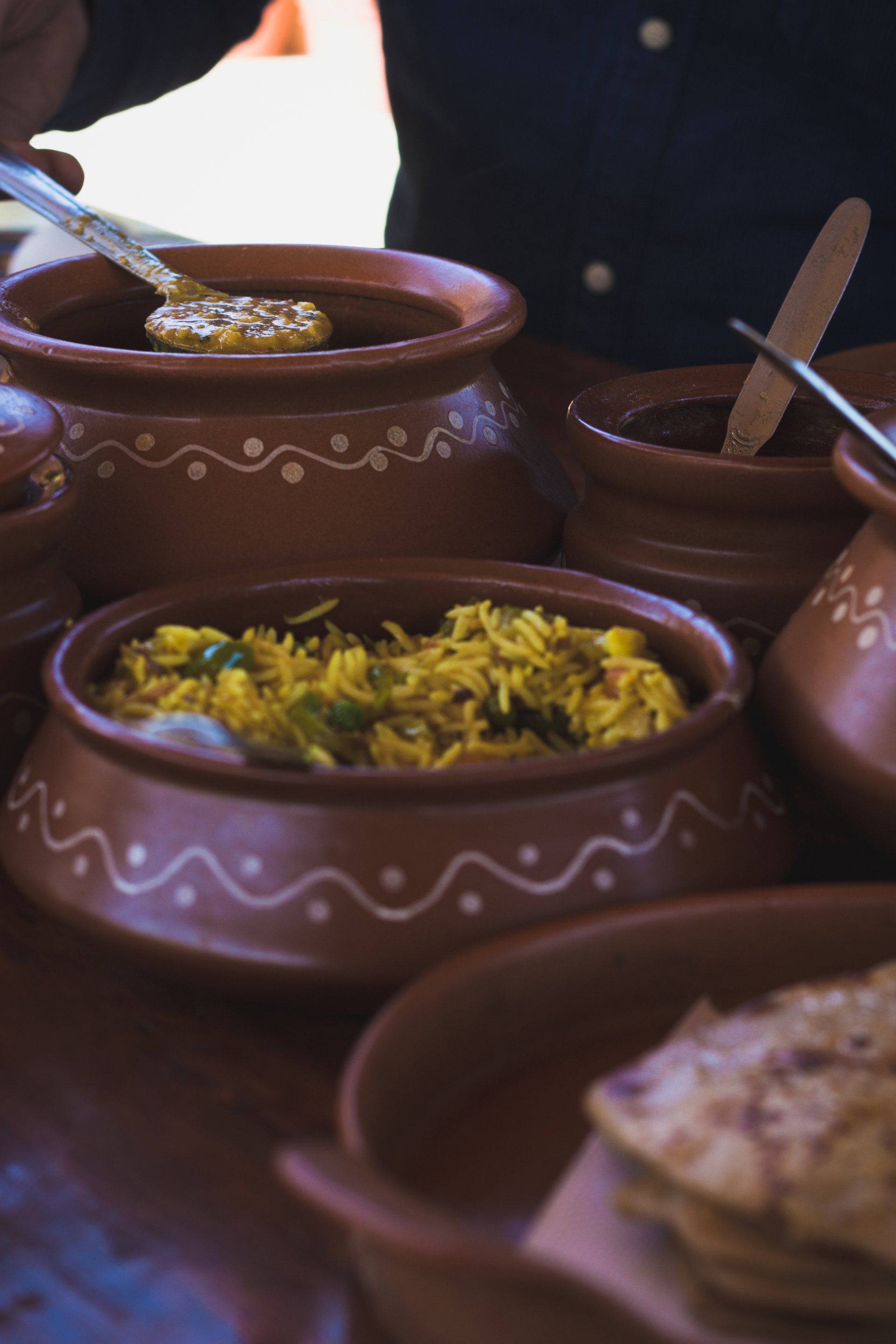 Clay bowls with yellow rice, other dishes, and a person scooping from one.