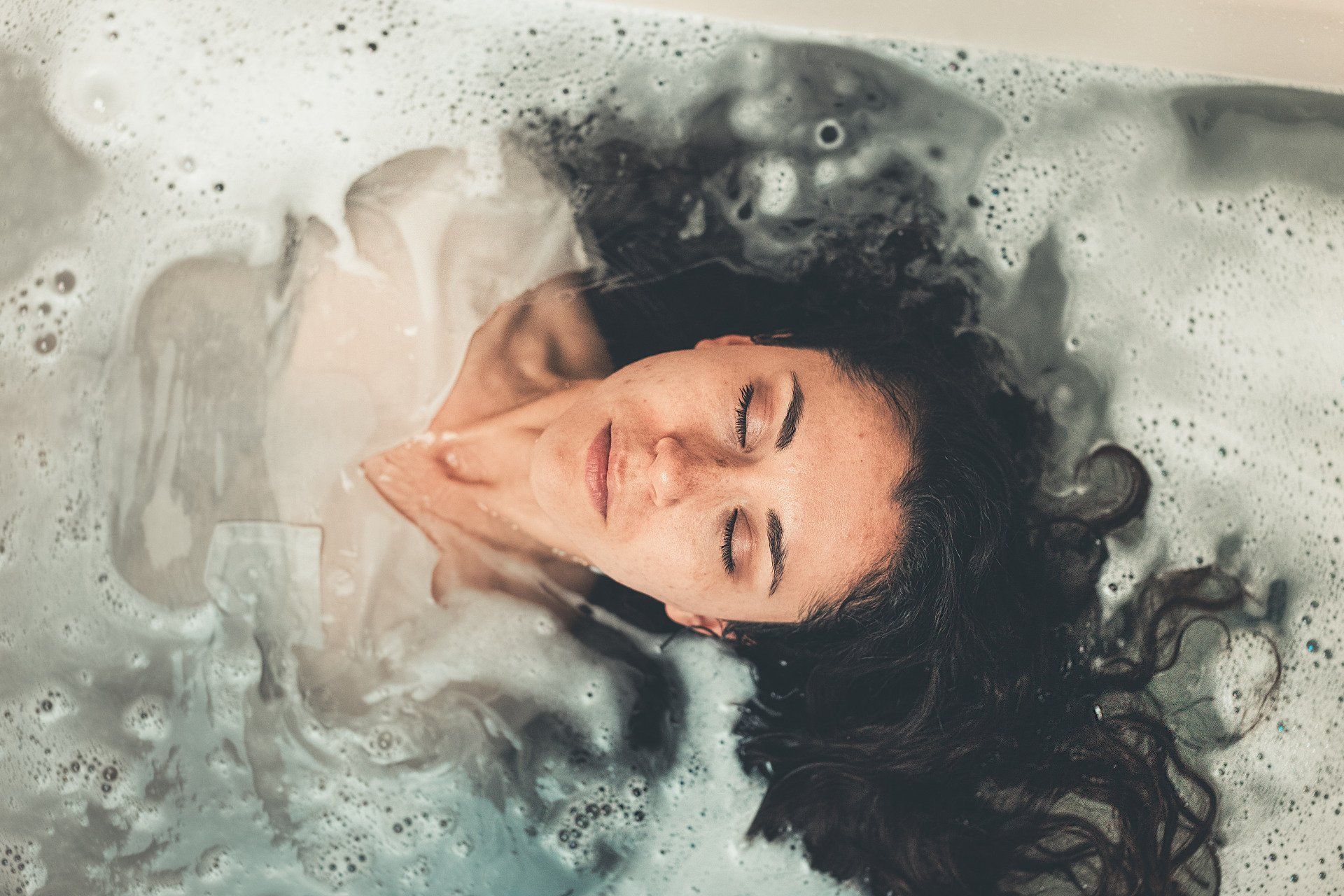 A woman is laying in a bathtub with her eyes closed.