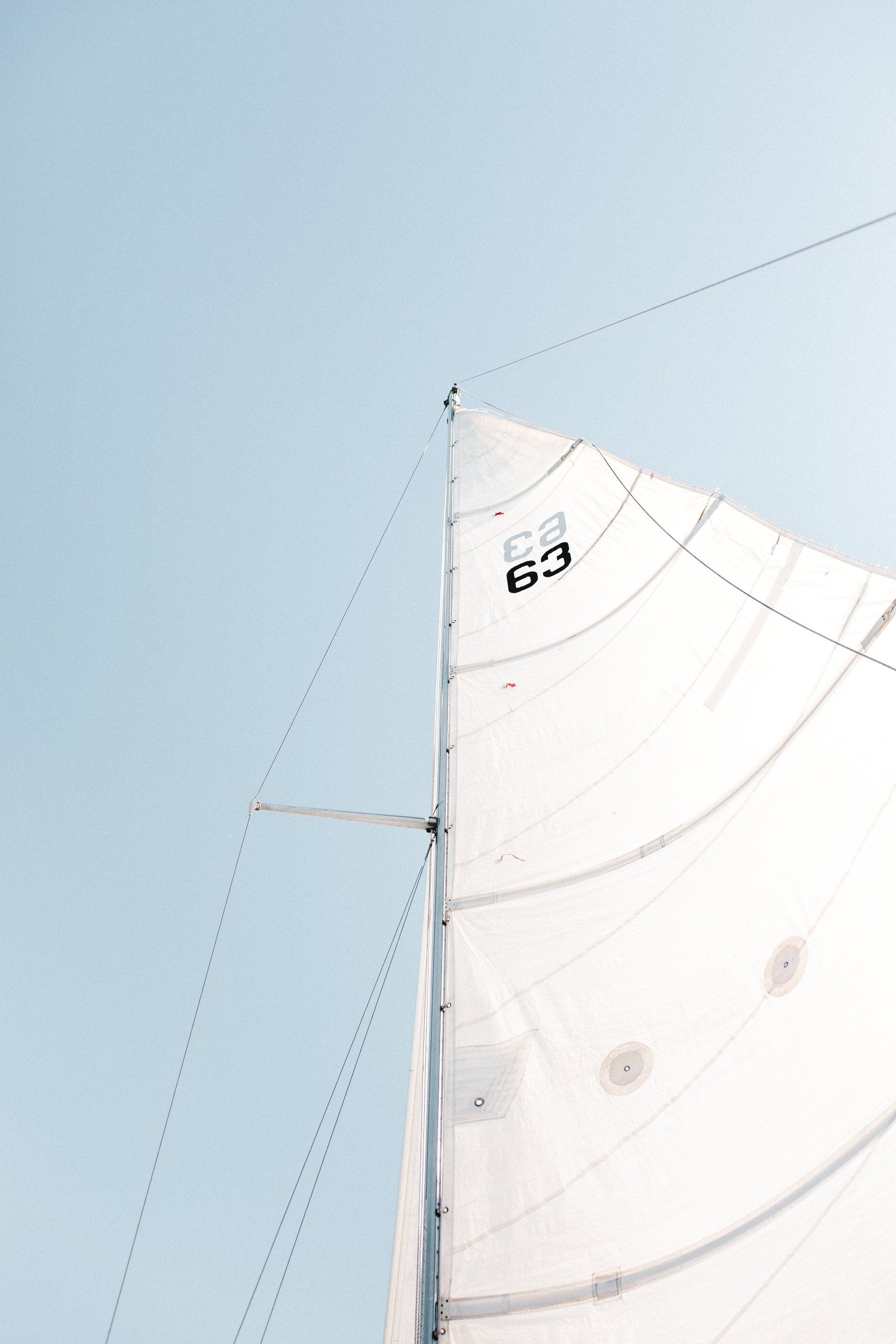 Un velero blanco navega contra un cielo azul pálido; un mástil y un aparejo son visibles.