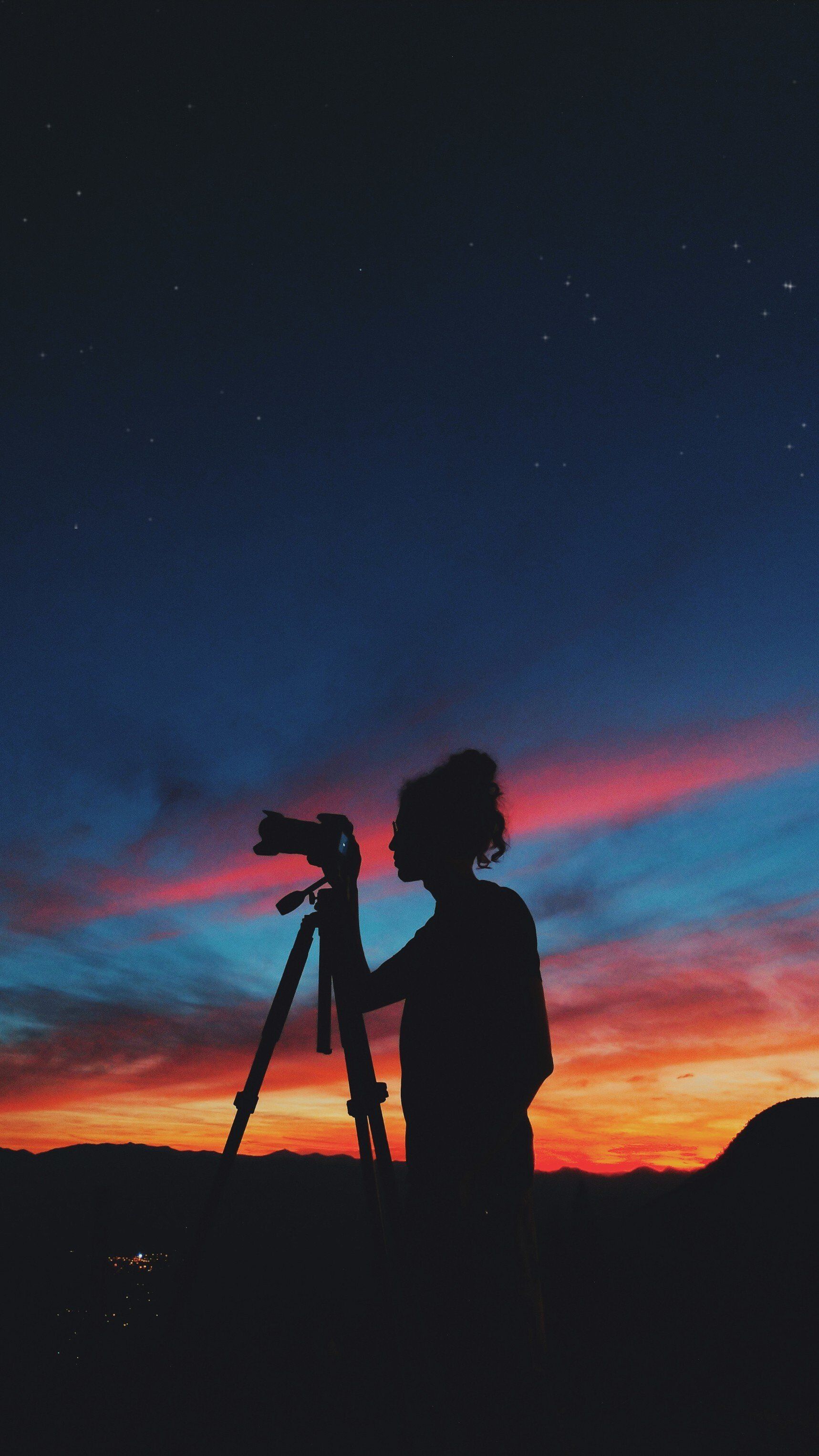 Une femme prend une photo d'un coucher de soleil avec un appareil photo sur un trépied.