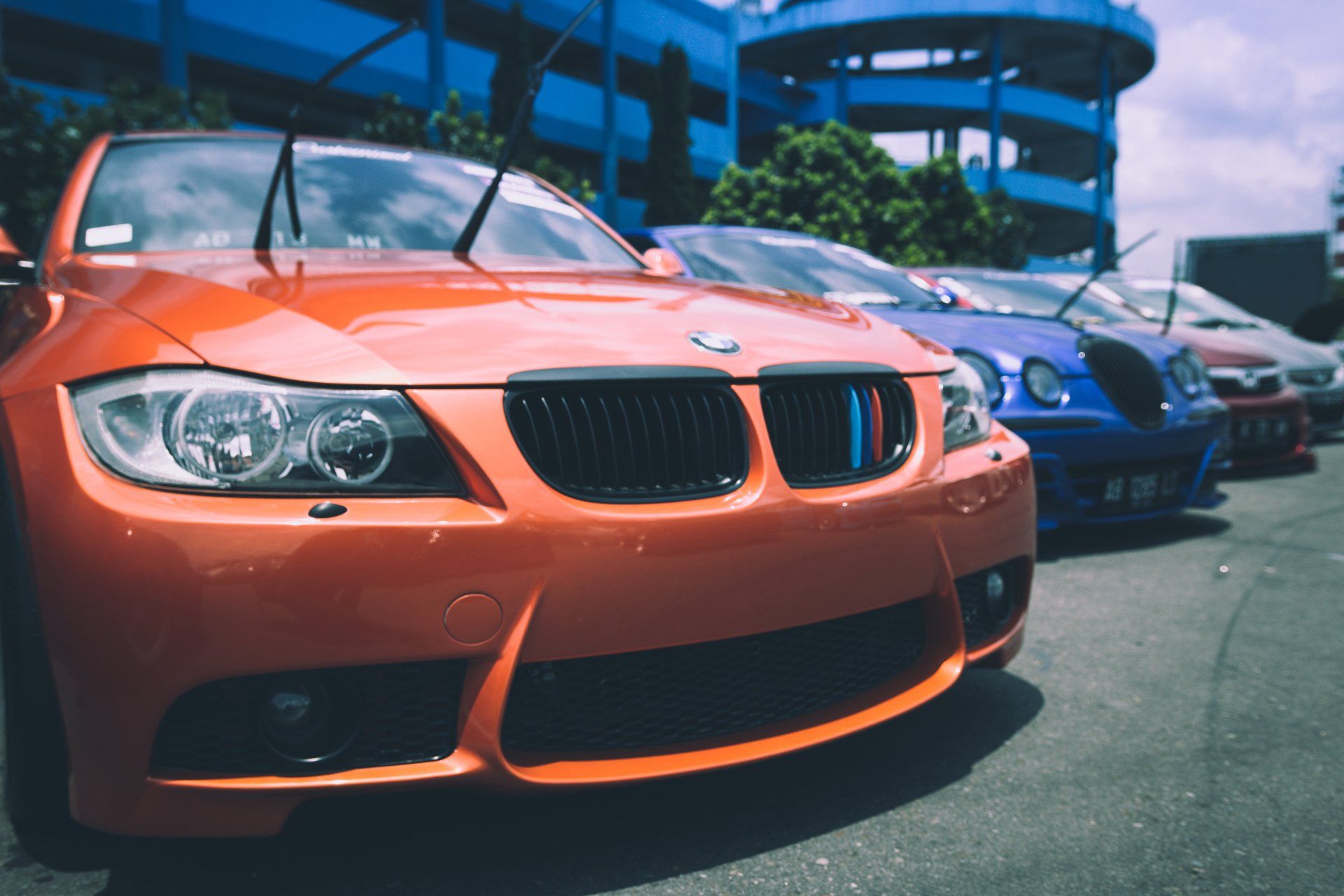 Orange BMW sports car parked in a row with other cars, a blue building in the background.