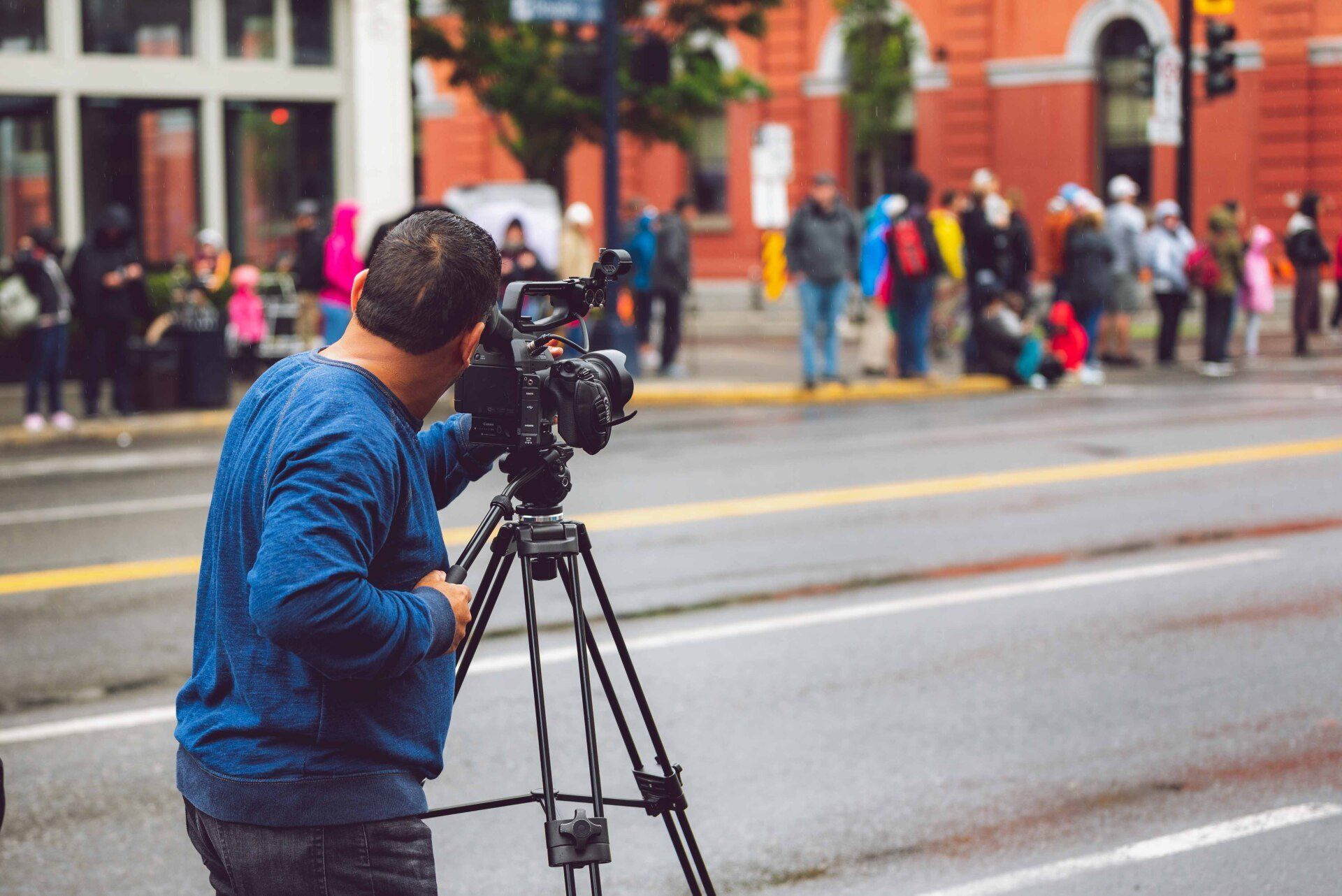 A man is holding a camera on a tripod in front of a crowd of people.