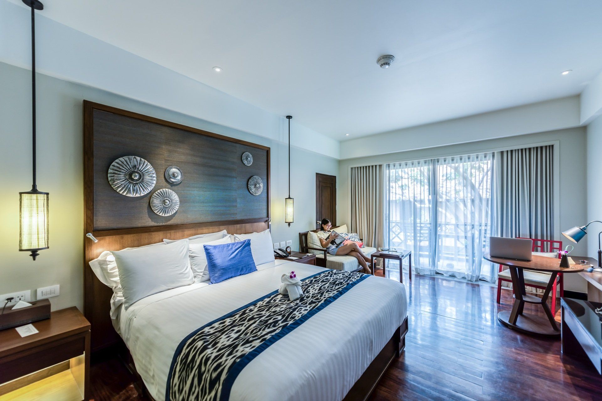 Quarto moderno com cama king-size, detalhes em azul, obras de arte na parede e portas de vidro deslizantes para uma varanda.