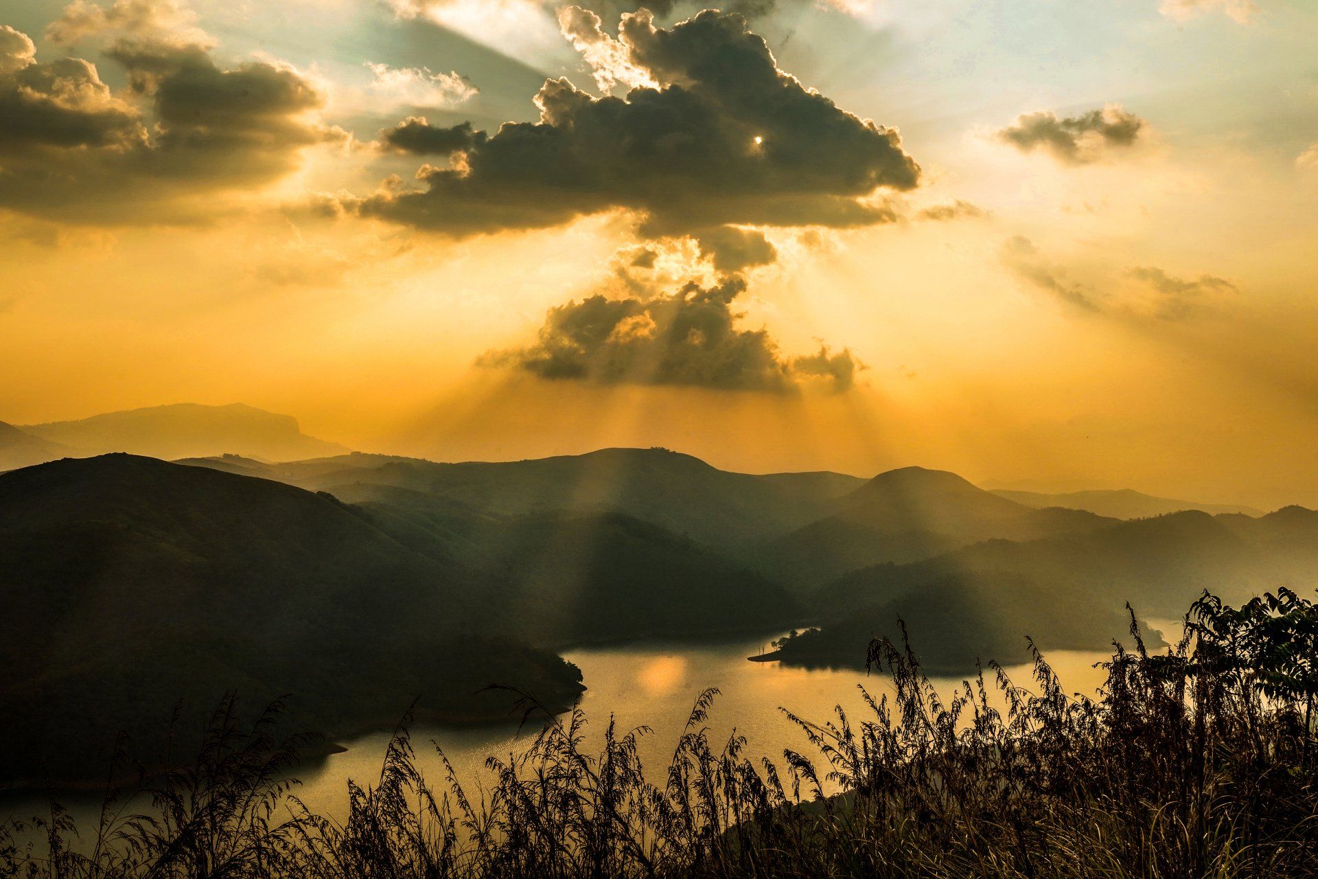 the sun is shining through the clouds over a lake surrounded by mountains .