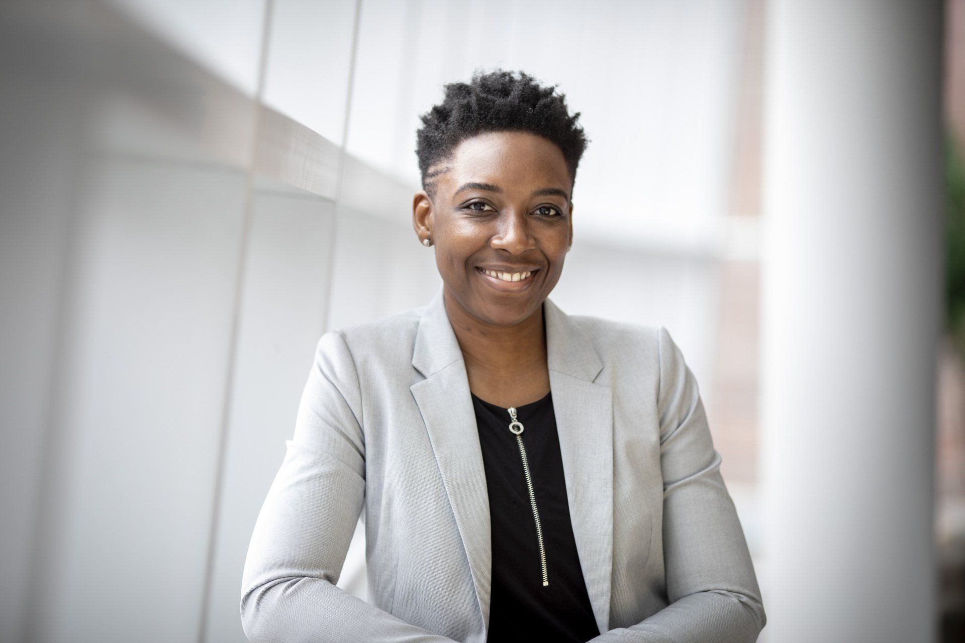 A woman in a grey jacket and black shirt is smiling for the camera.