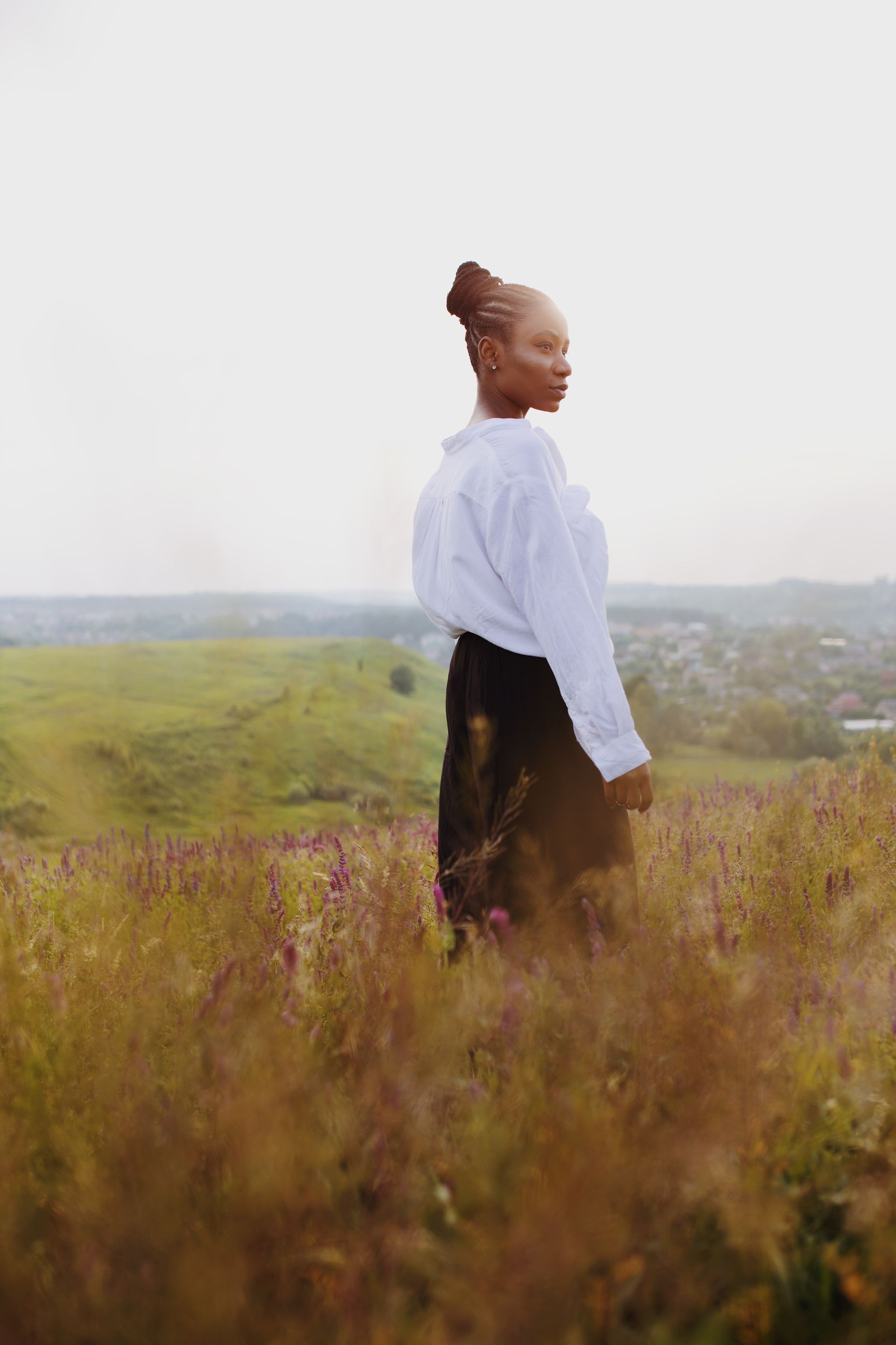 A woman in a white shirt and black skirt is standing in a field of tall grass.