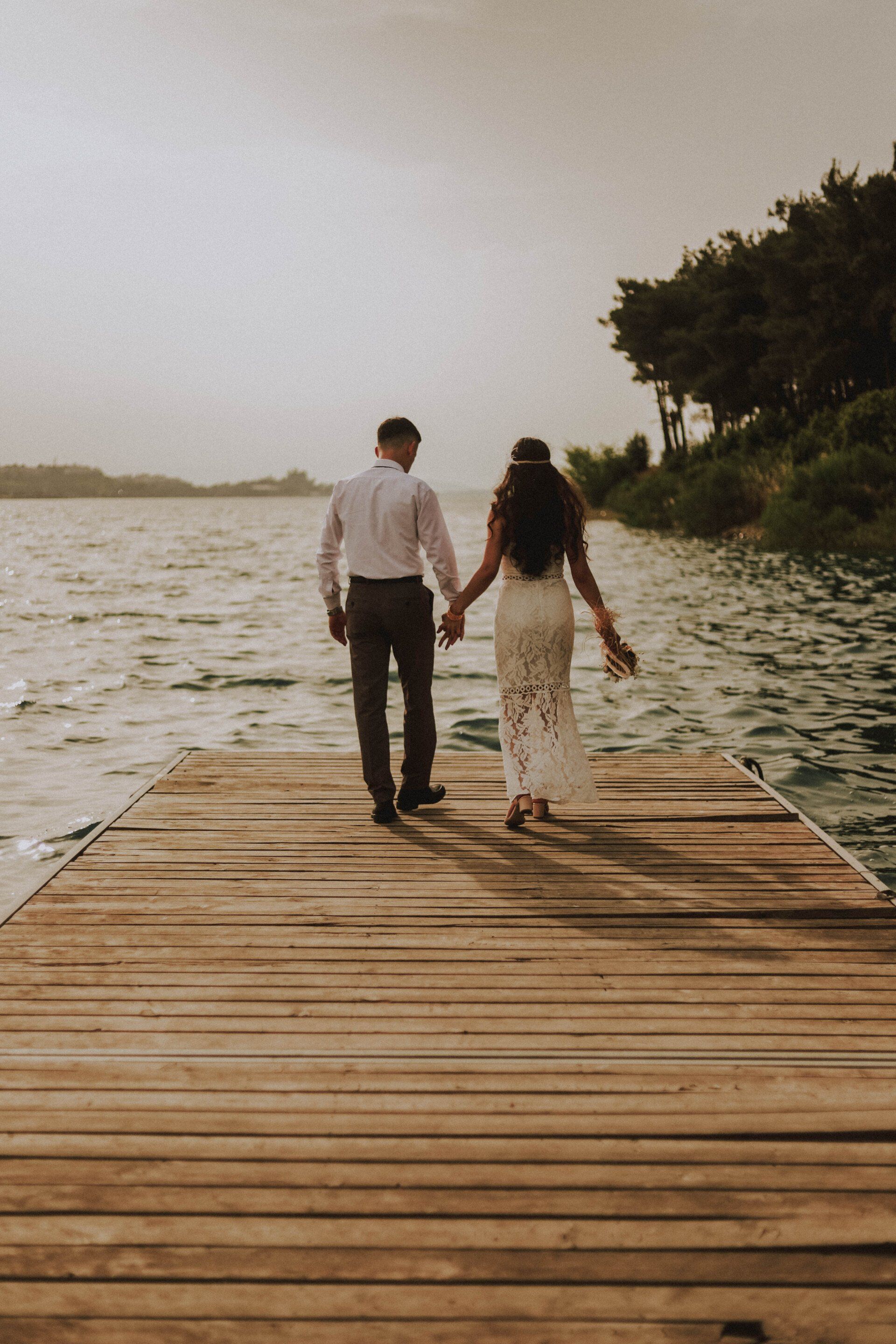 two people walking on a pier that are in wedding clothes