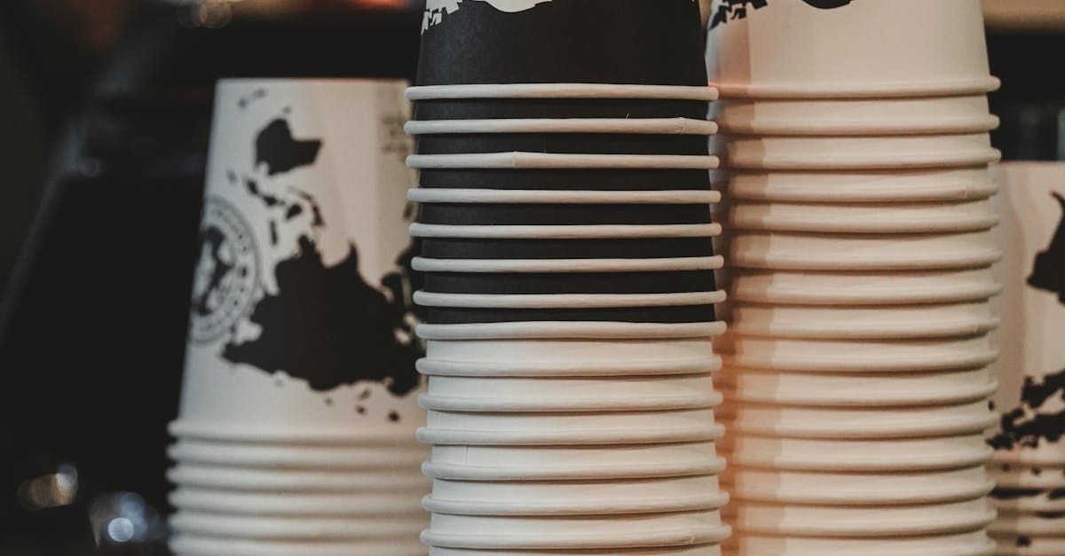 Stacks of white paper cups with black and beige patterns, arranged in a row on a counter.