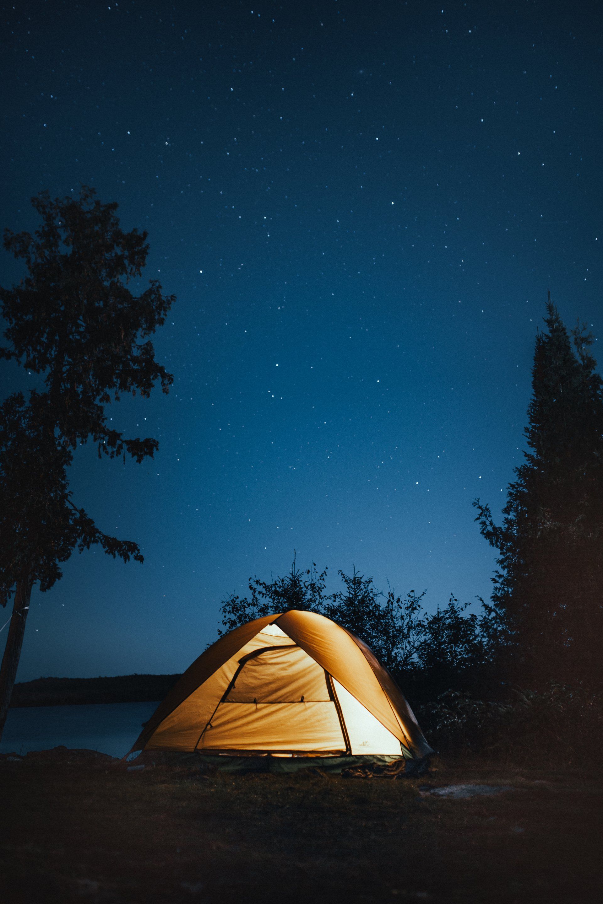 A tent is lit up at night under a starry sky.
