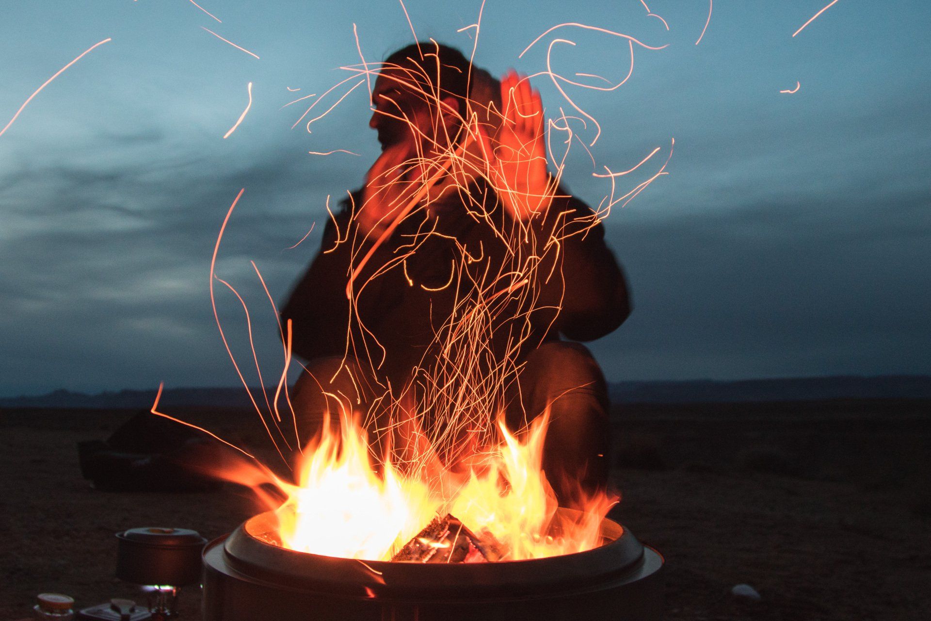A man is sitting in front of a fire with sparks coming out of it