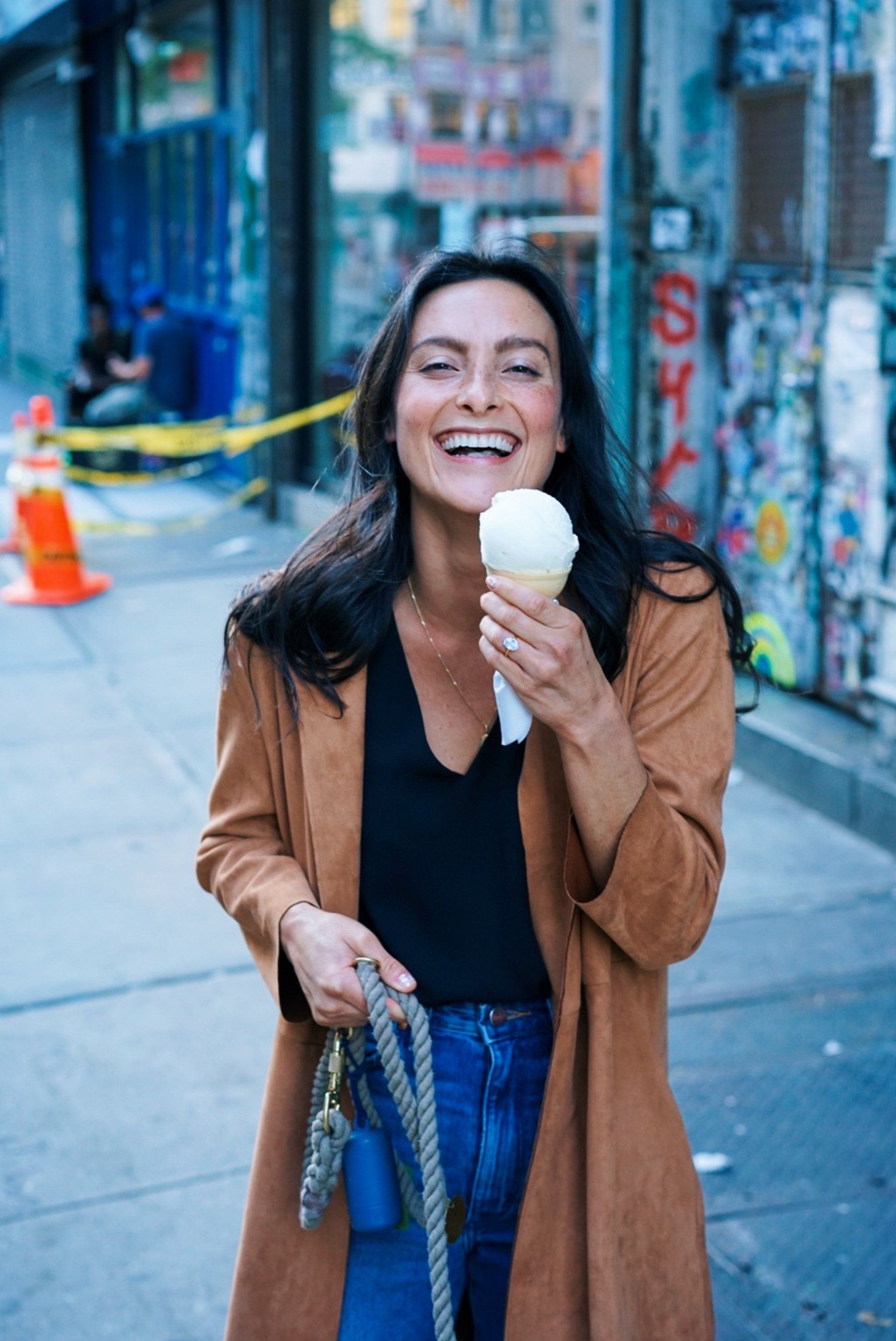 A woman is eating an ice cream cone on the sidewalk.