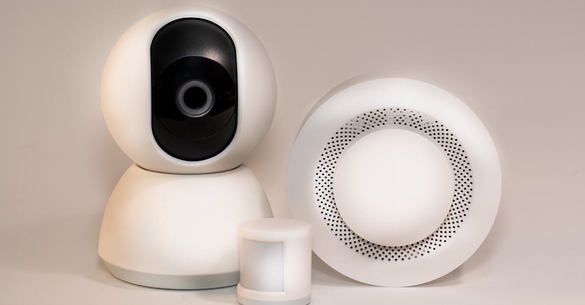 A security camera , motion sensor , and smoke detector are sitting on a table.