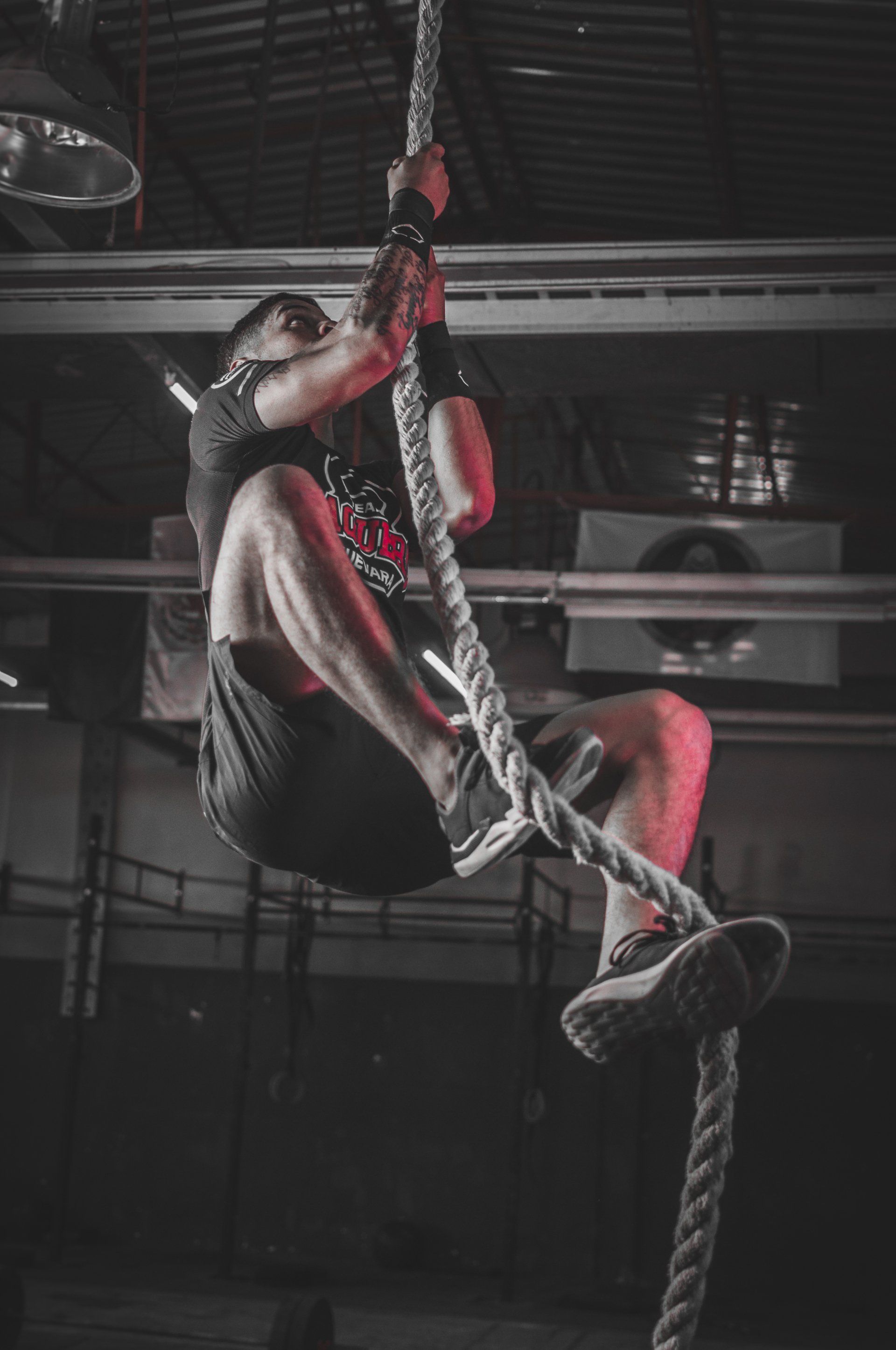 A man is climbing a rope in a gym.