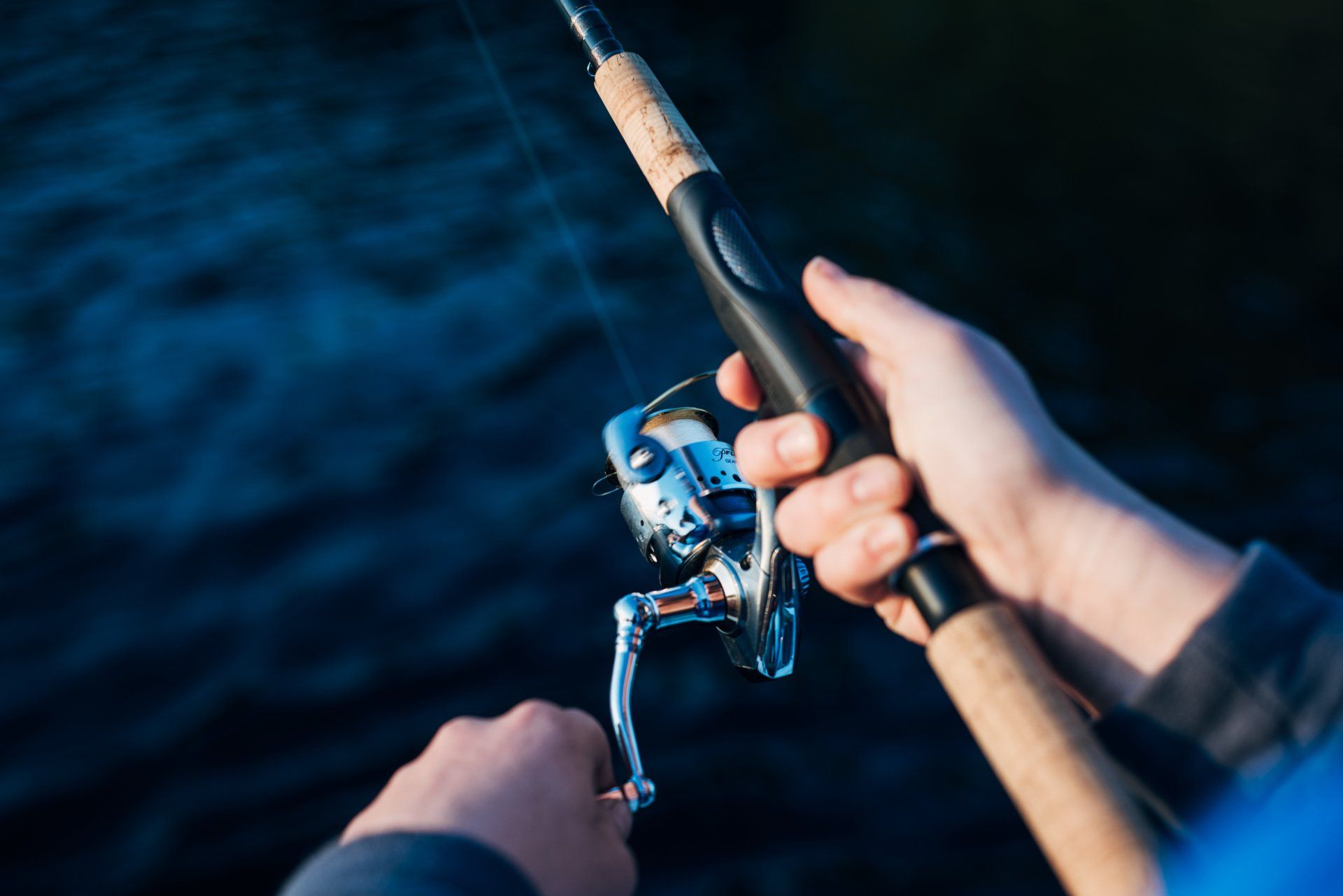Hands holding a fishing rod and reel over dark blue water