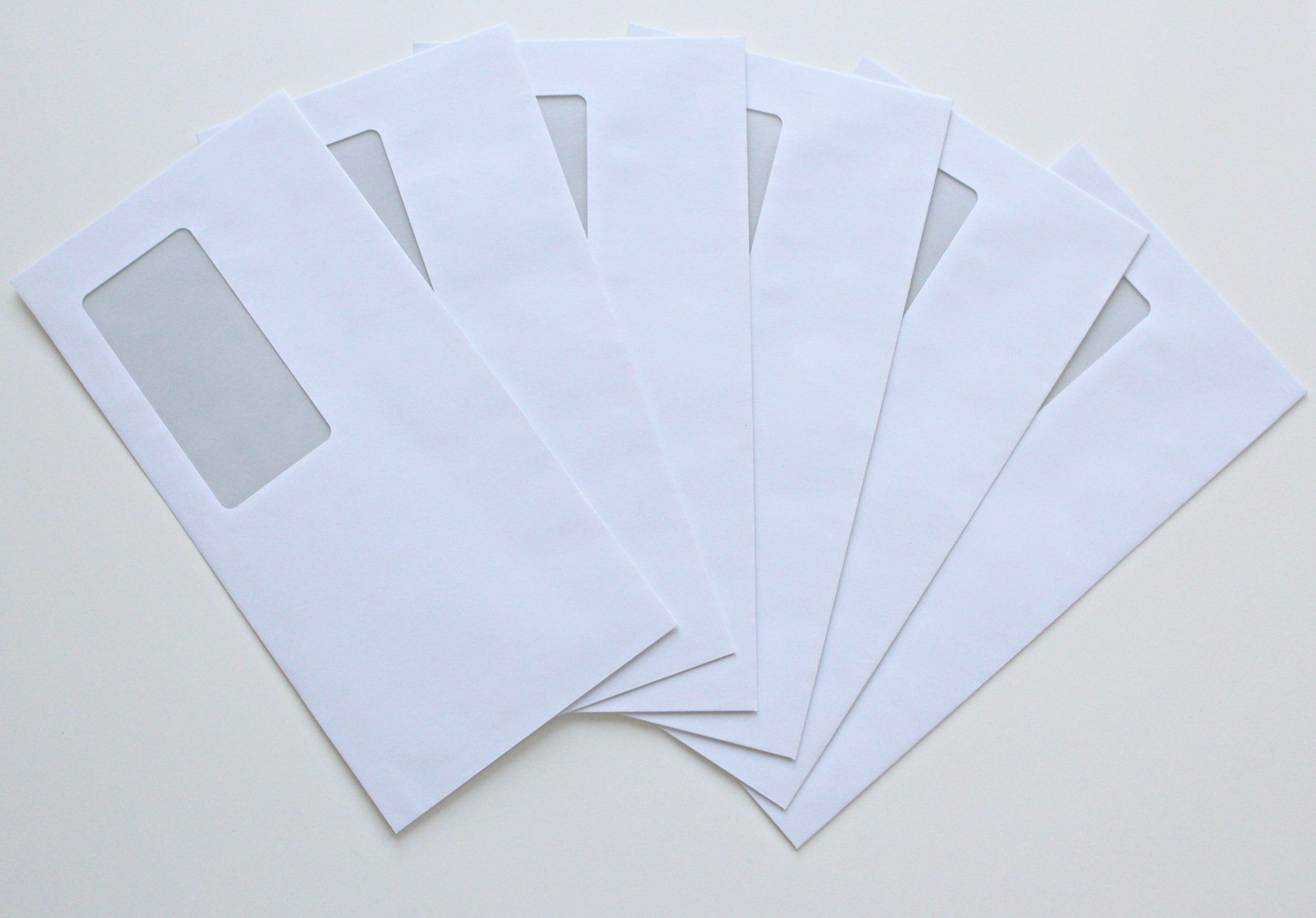 White envelopes with clear address windows fanned out on a white surface.