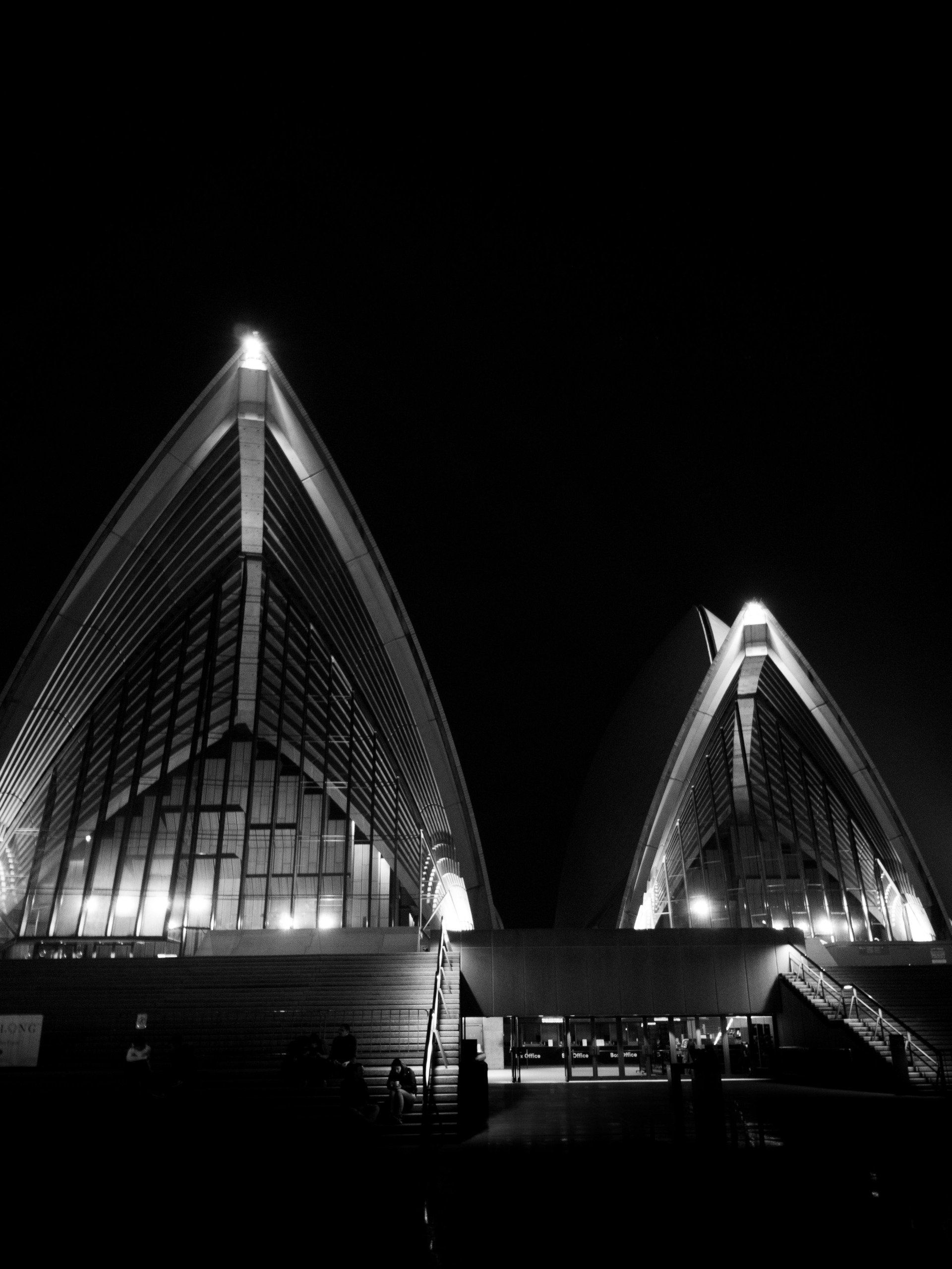 A Ópera de Sydney à noite, iluminada contra um céu escuro.