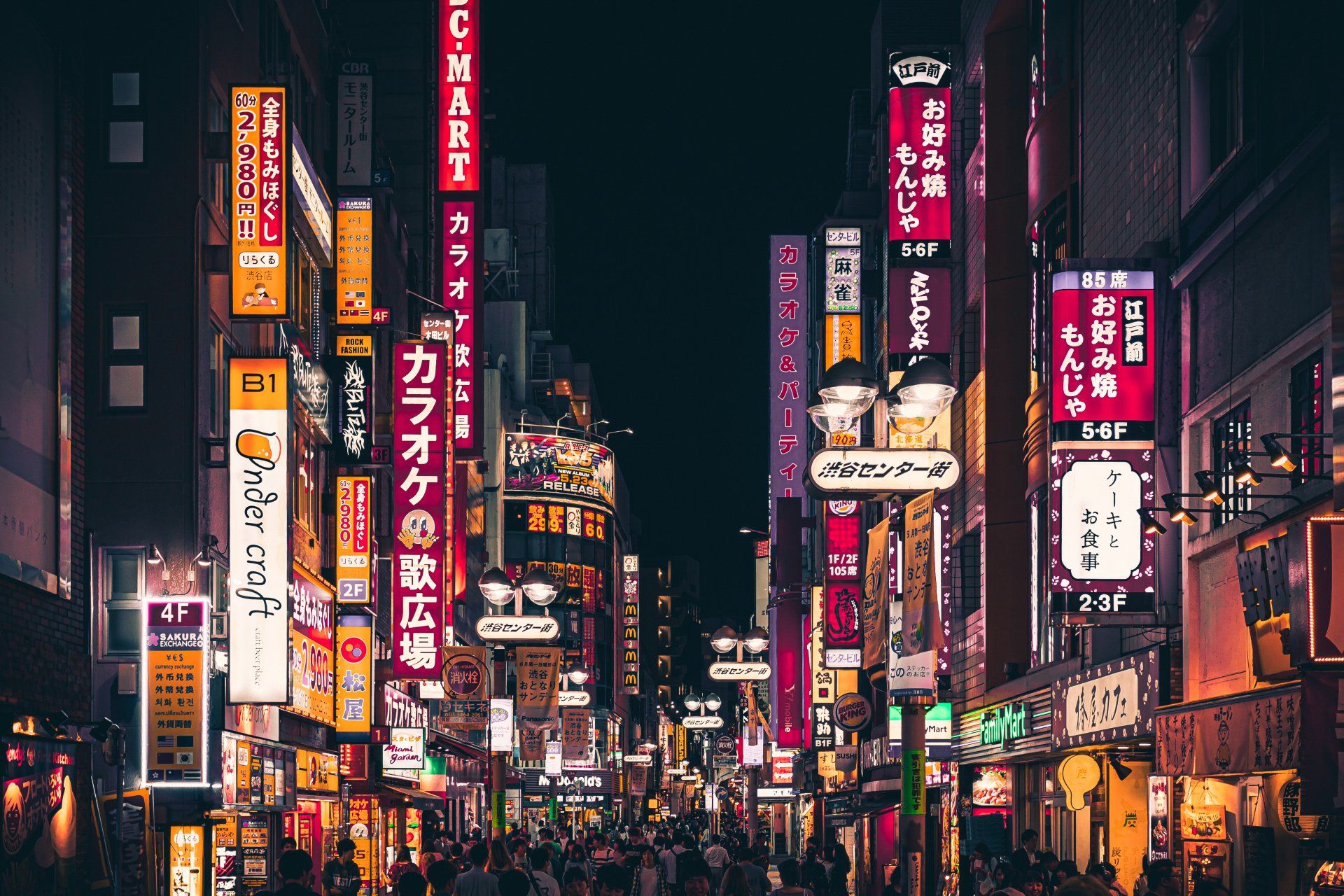 Bright neon signs illuminate a crowded street in Tokyo at night.