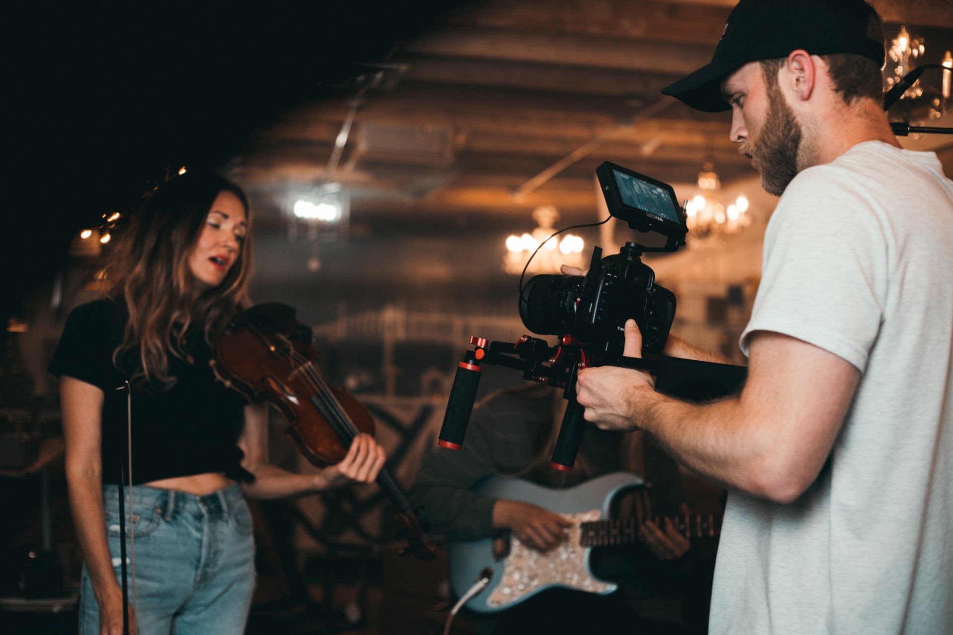 A man is holding a camera while a woman plays a violin.