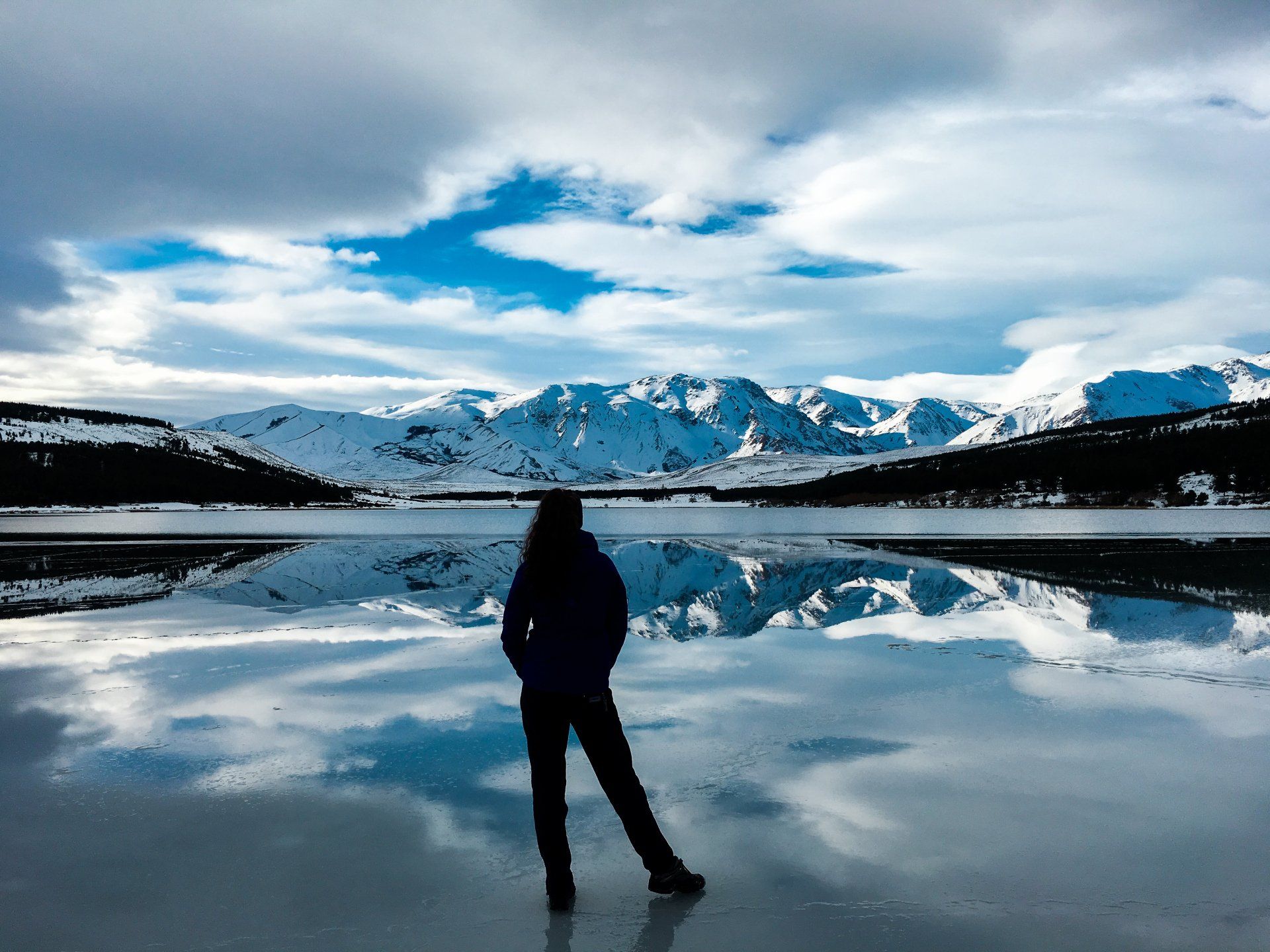 A person is standing on a frozen lake with mountains in the background.