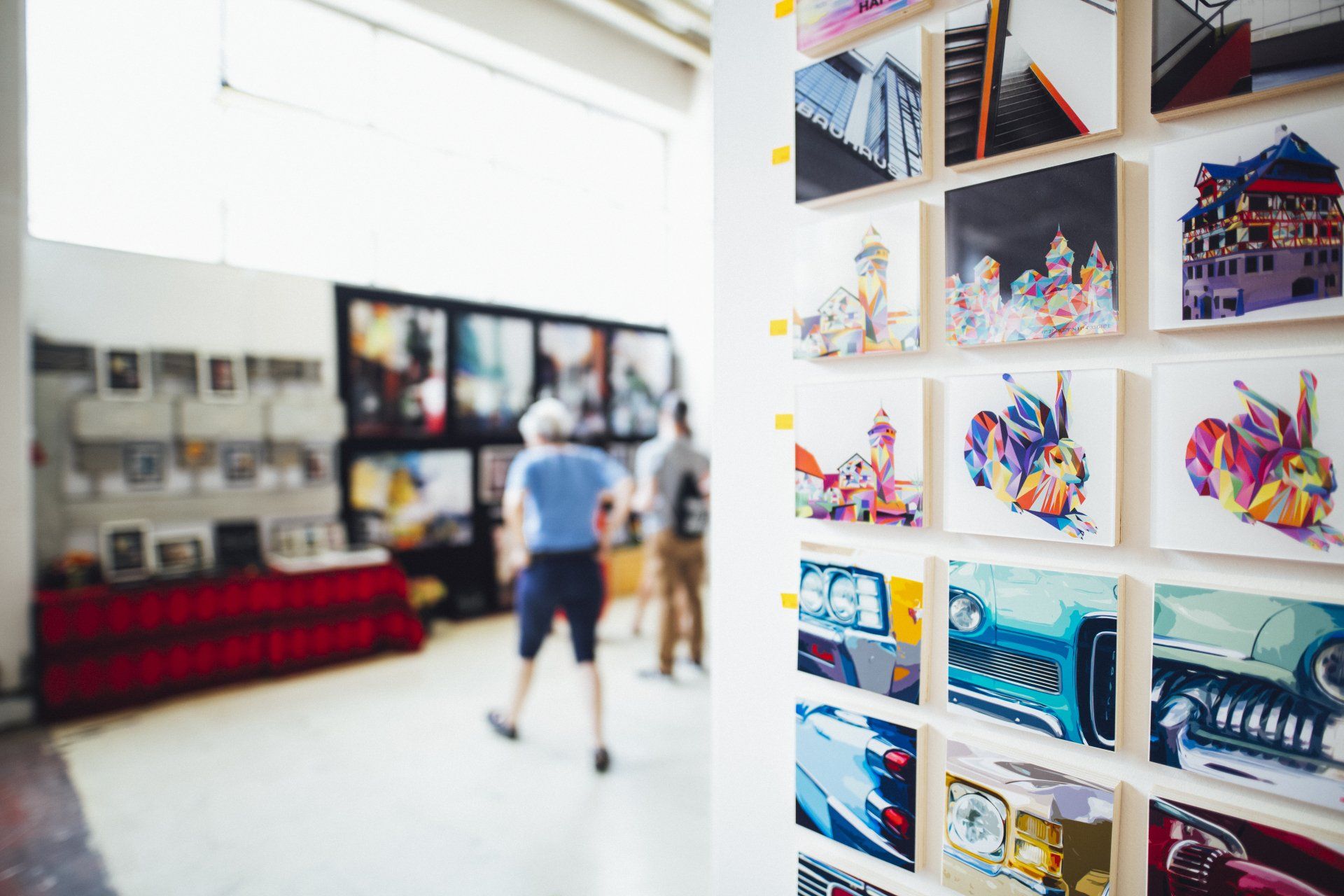 Art gallery interior with a wall of colorful square paintings, and people viewing the artwork.