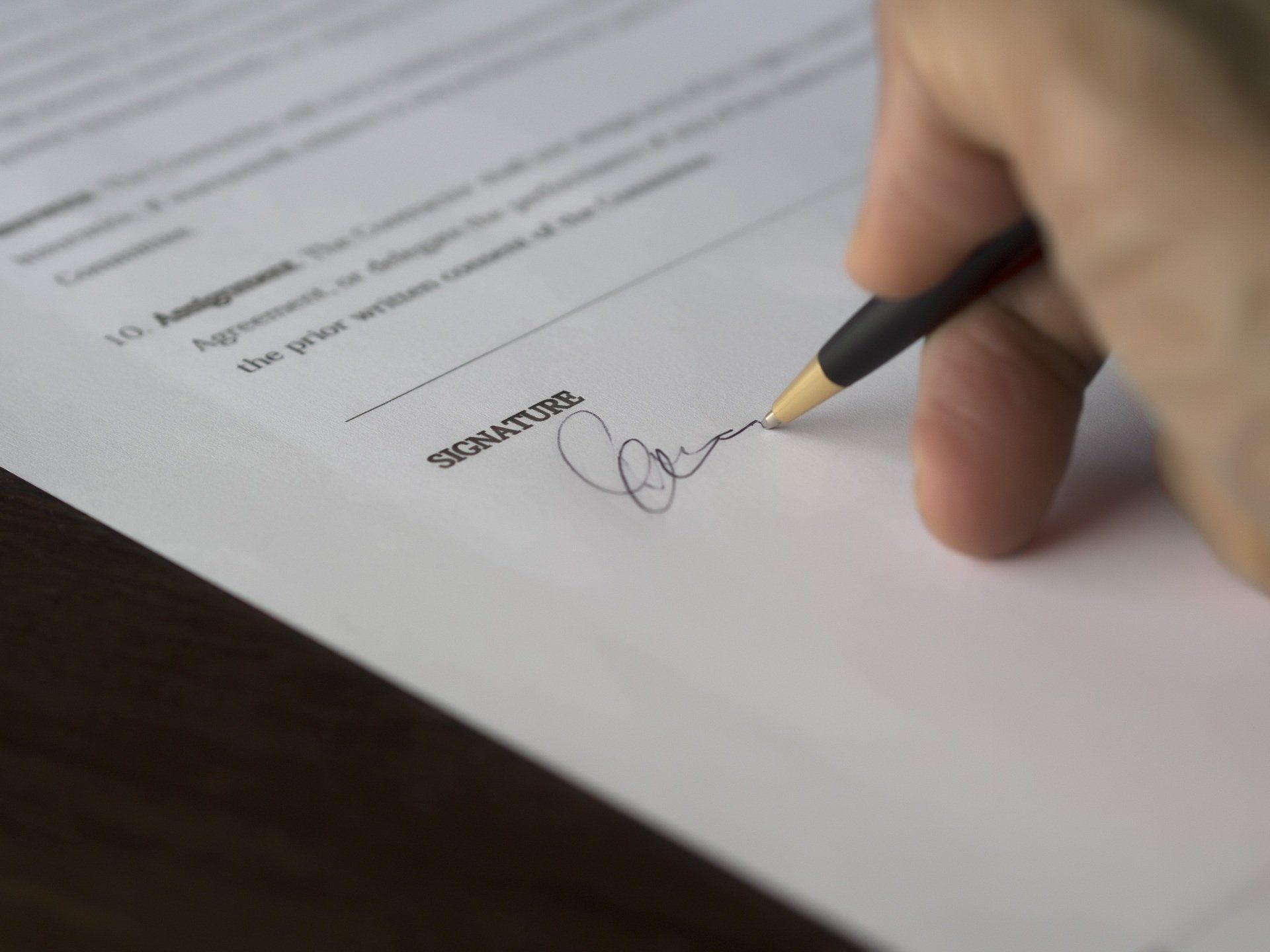 A hand holding a pen signs a document on a white paper.