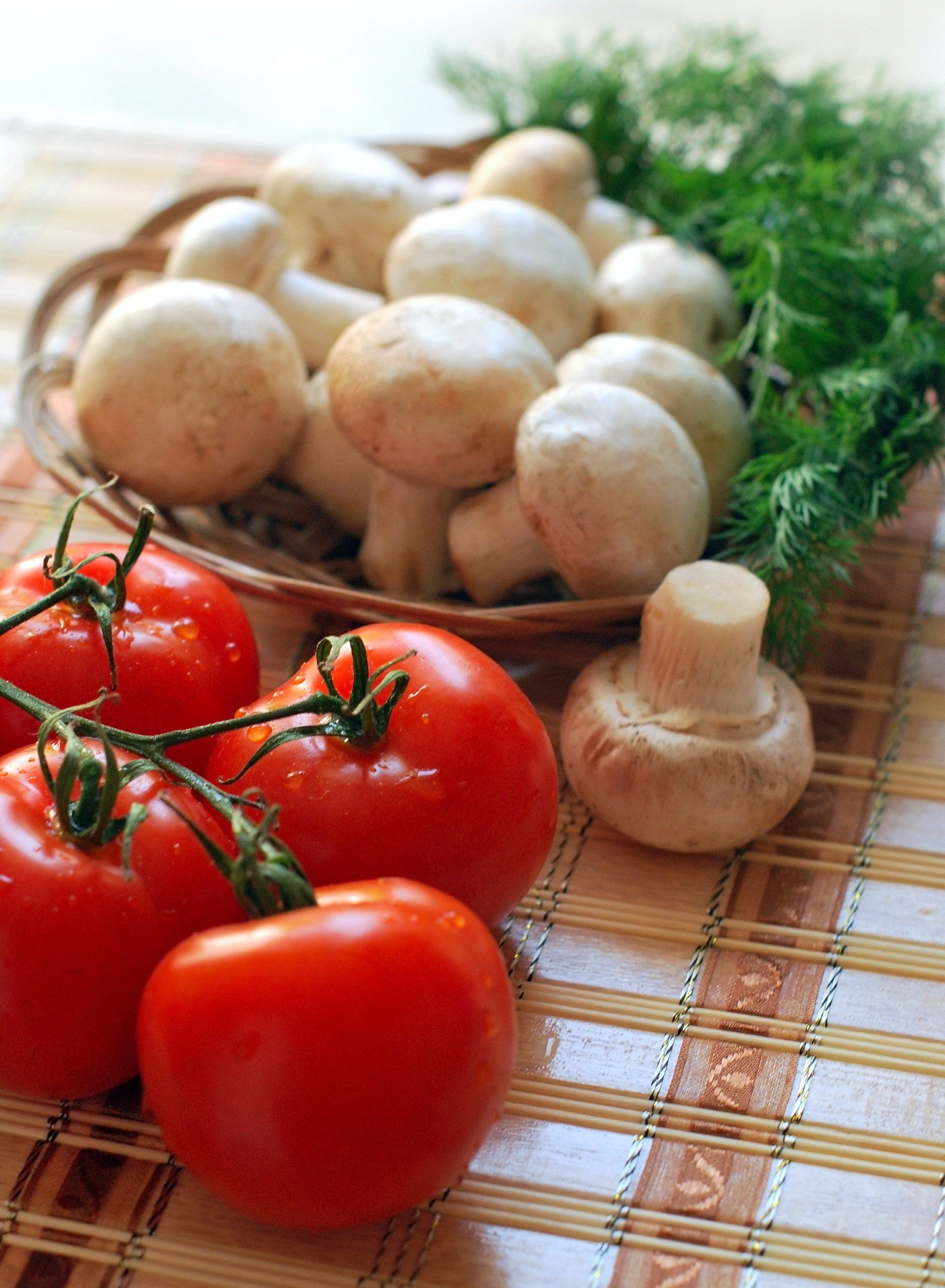 Tomatoes and mushrooms are on a bamboo mat on a table.