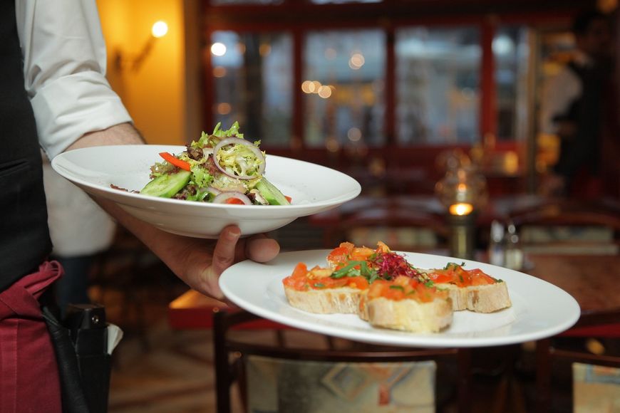 Waiter holding two plates of food in a restaurant setting: salad and bruschetta.