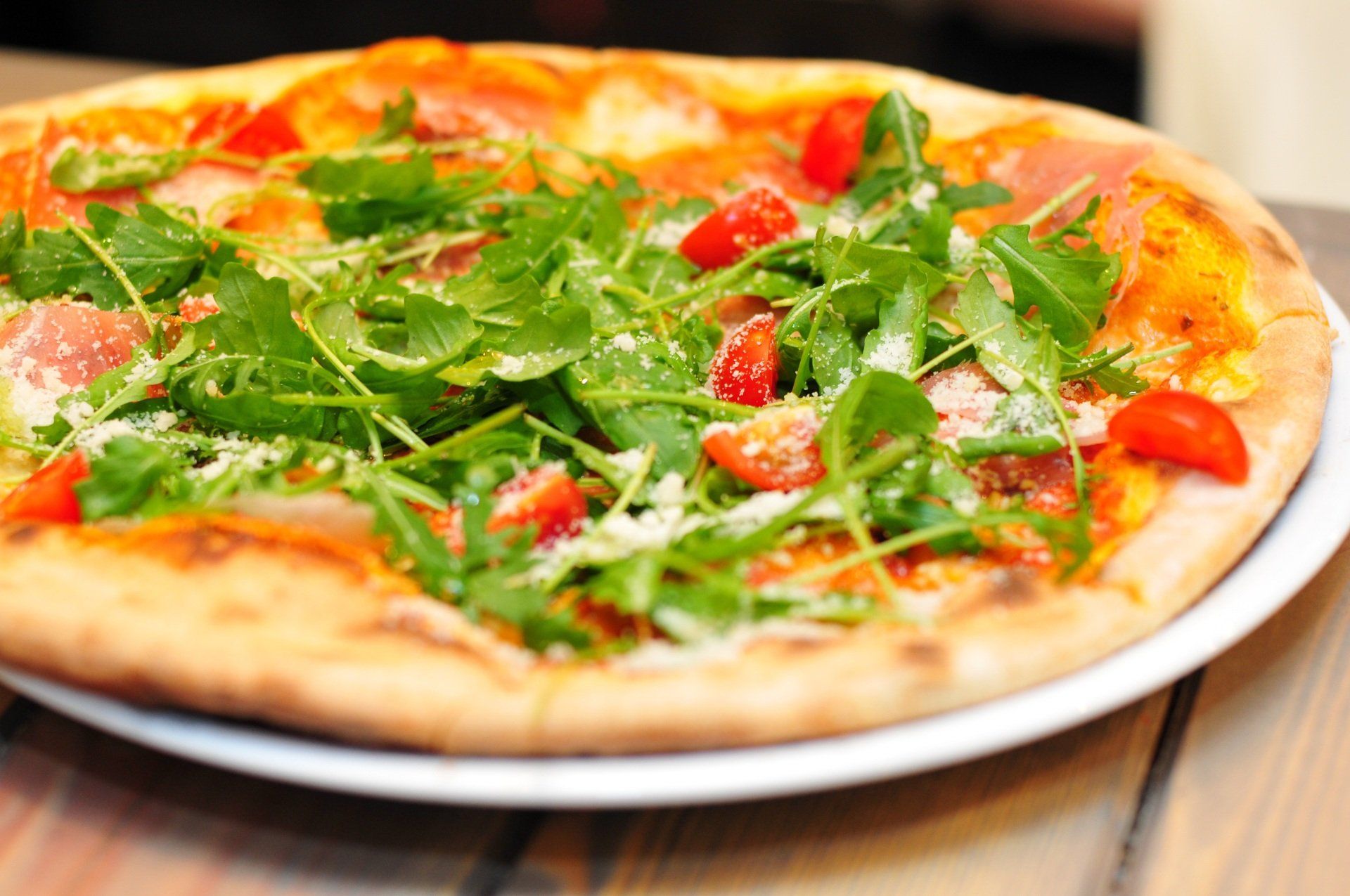 Pizza topped with arugula, cherry tomatoes, and cheese on a white plate.