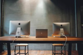 Two apple computers and a laptop are sitting on a wooden desk.