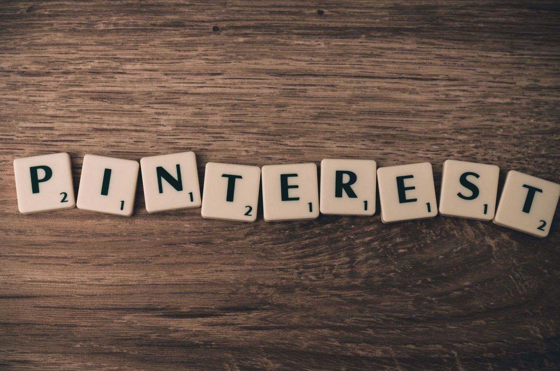 The word pinterest is written in scrabble tiles on a wooden table.