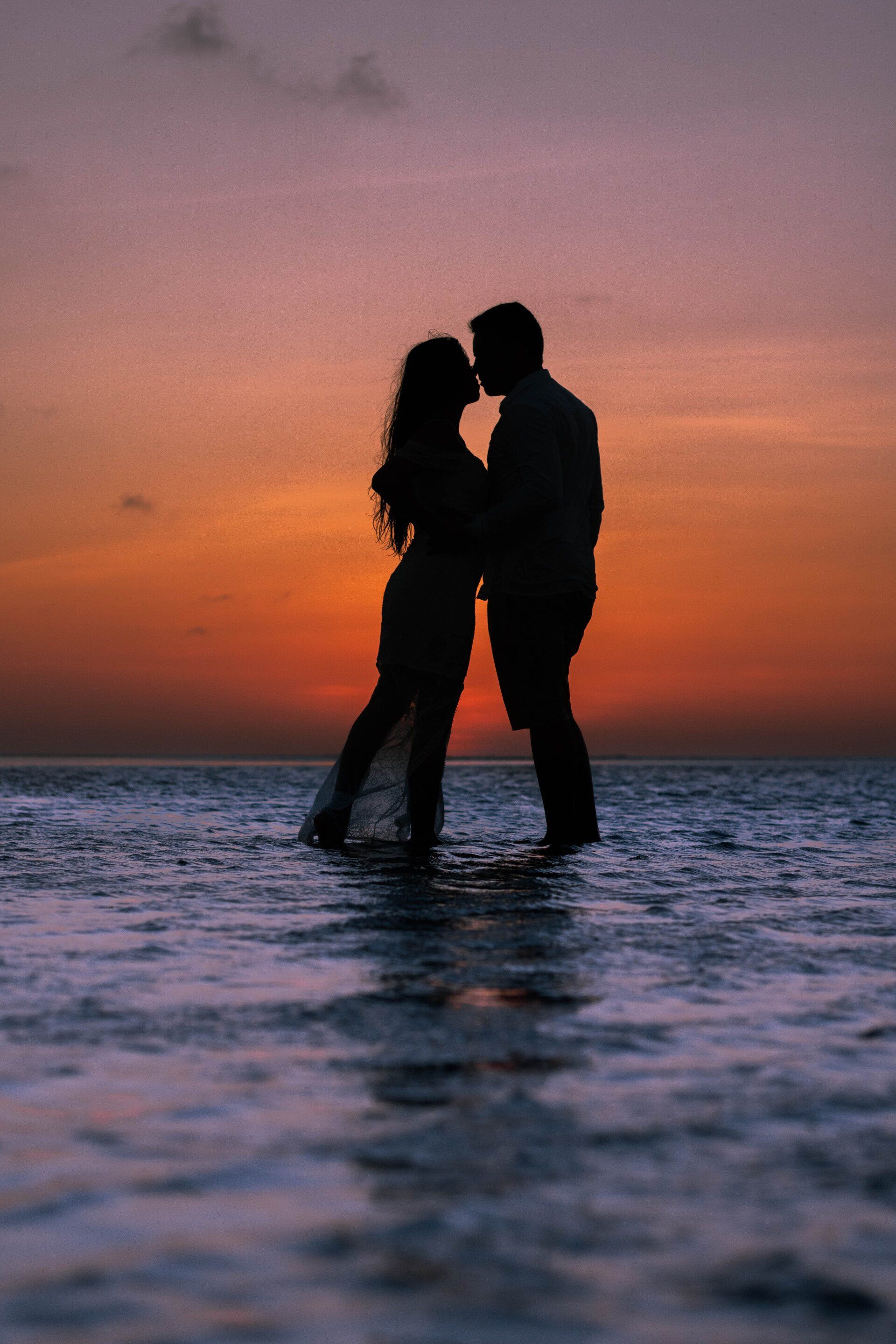 Um homem e uma mulher estão se beijando no oceano ao pôr do sol.