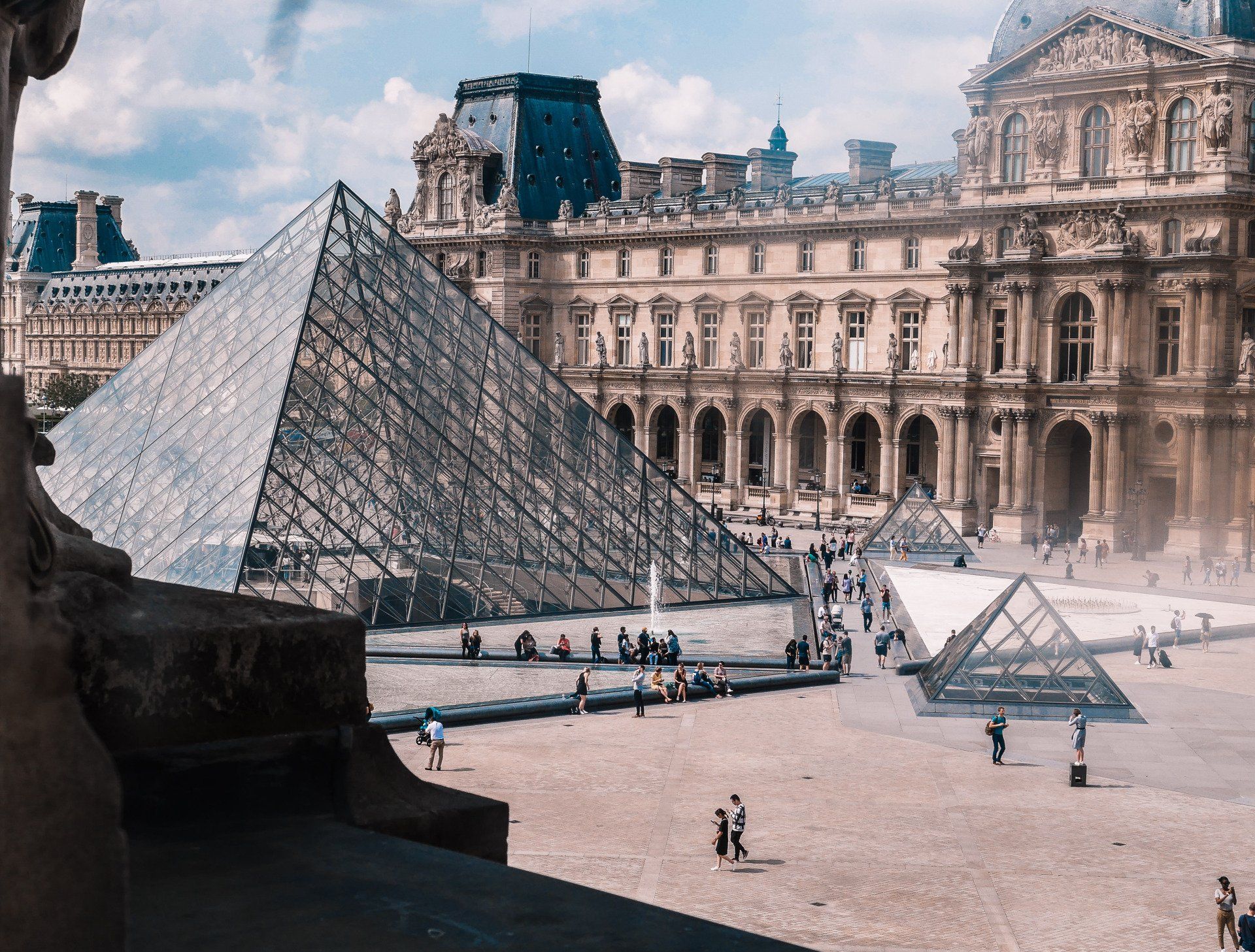 The glass Louvre Pyramid stands in a large courtyard in front of the historic Louvre Palace museum in Paris.