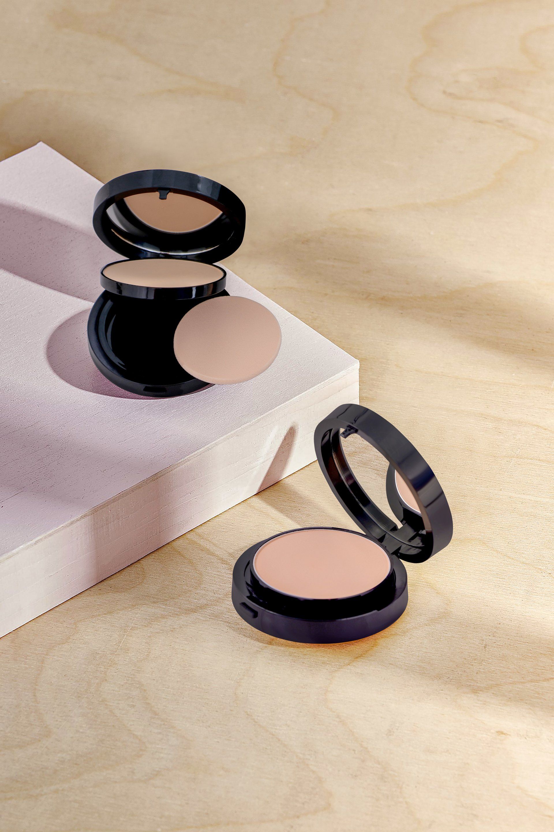 Two compacts of powder are sitting on top of each other on a table.