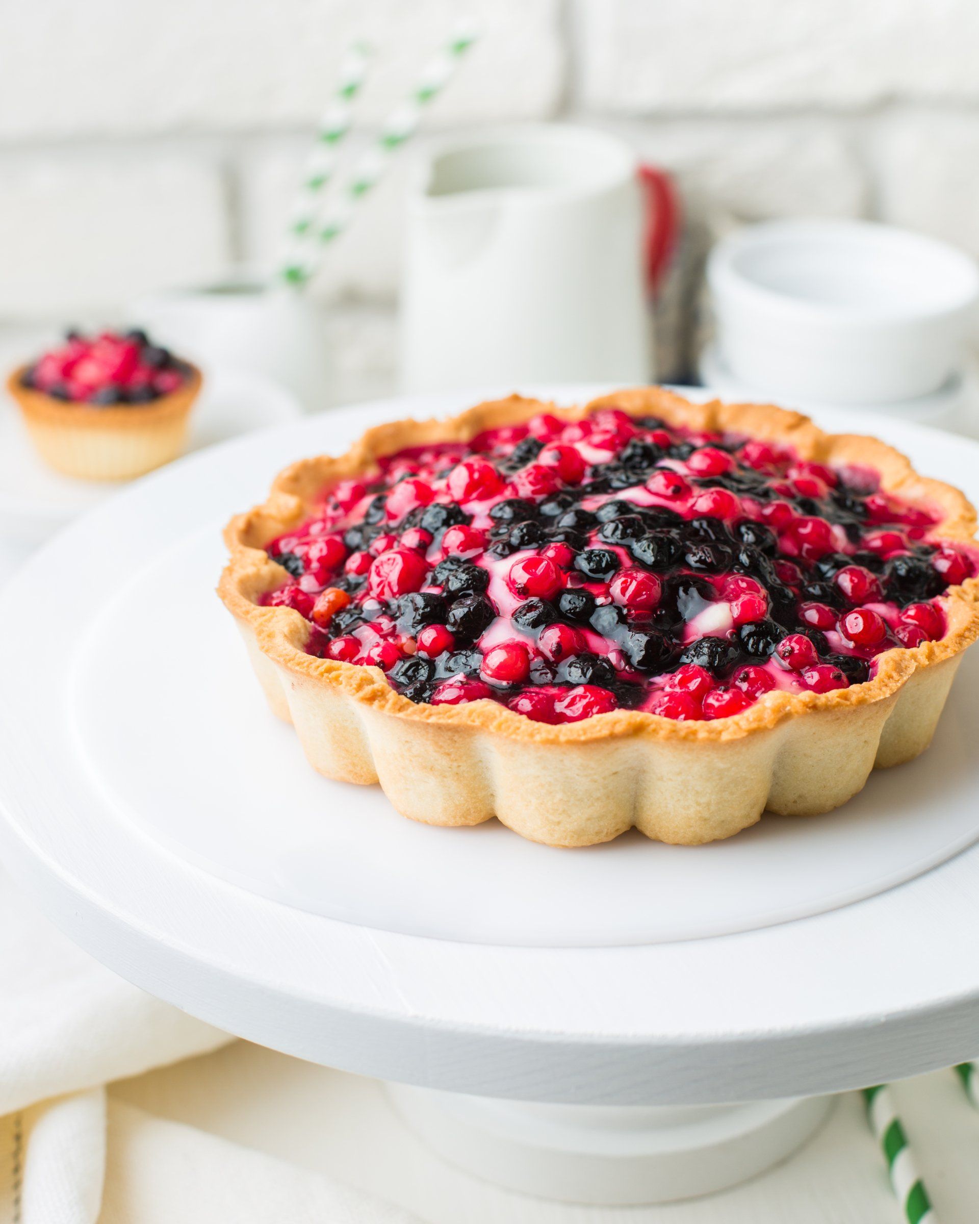Crostata ai frutti di bosco su un'alzata bianca. Bacche rosse e nere riempiono la base di pasta.