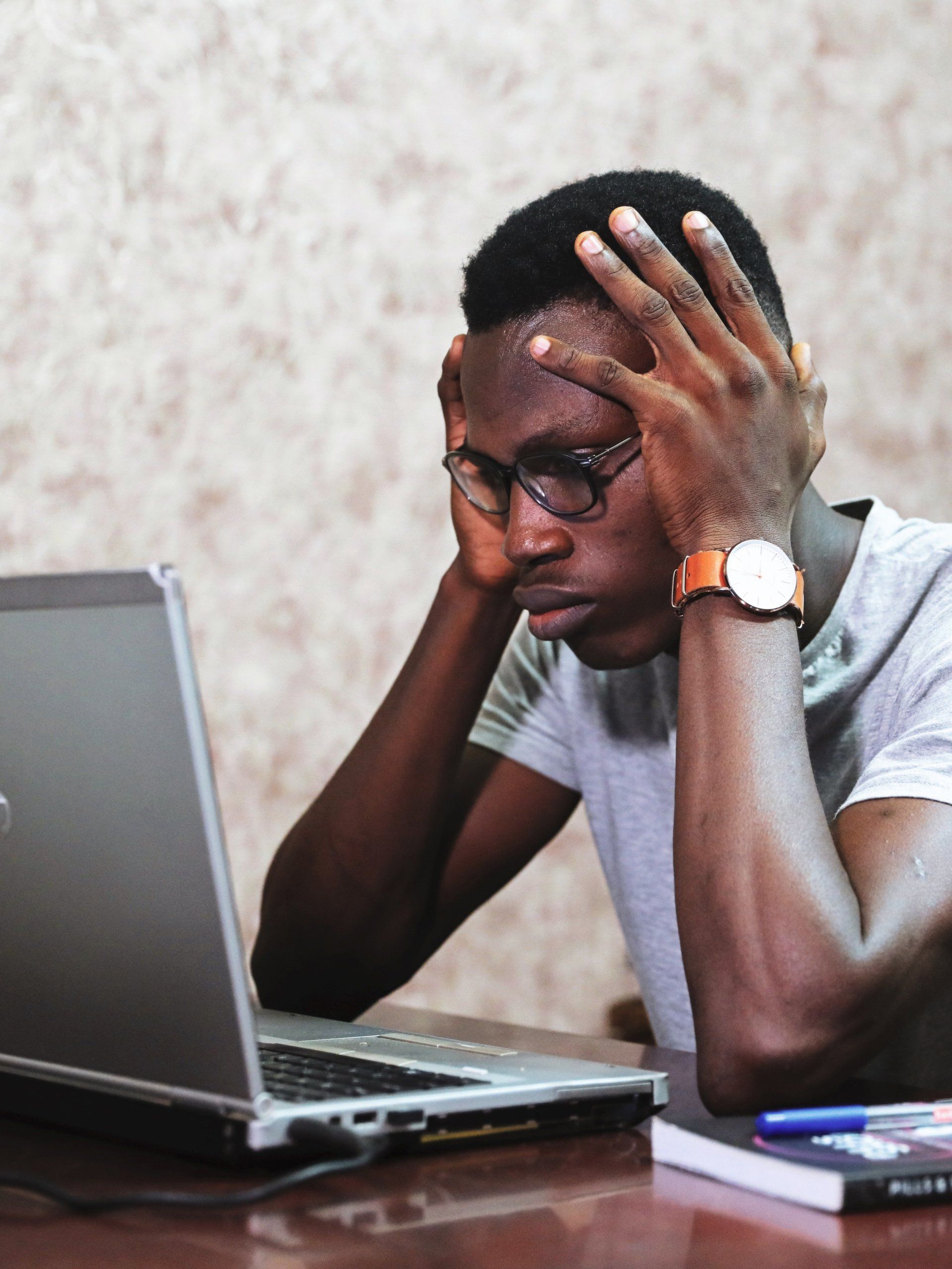 a man sitting in front of a laptop with his hands on his head