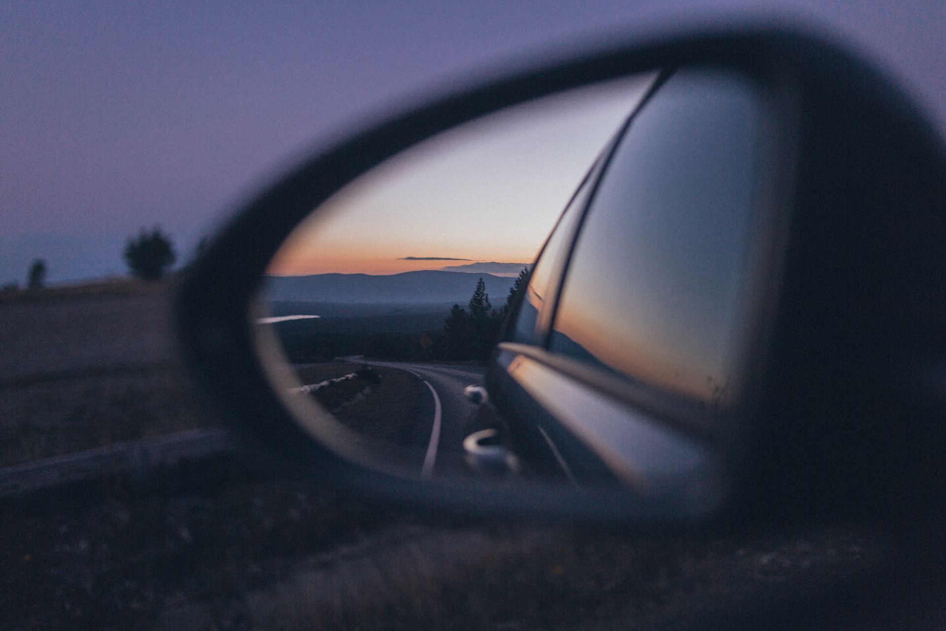 A car is driving down a curvy road at sunset.